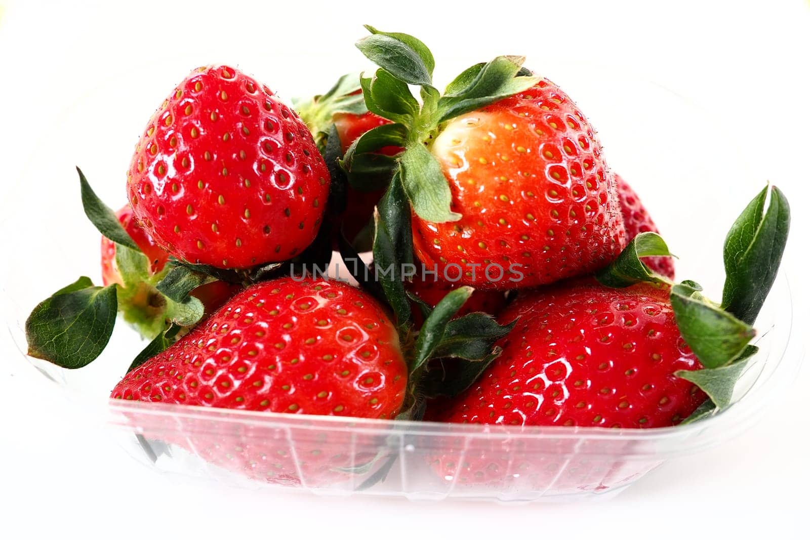 Ripe strawberries in a plastic package on a white background. Delicious fresh berries in a container for sale to customers. Keeping food fresh. Healthy food, vitamins and microelements