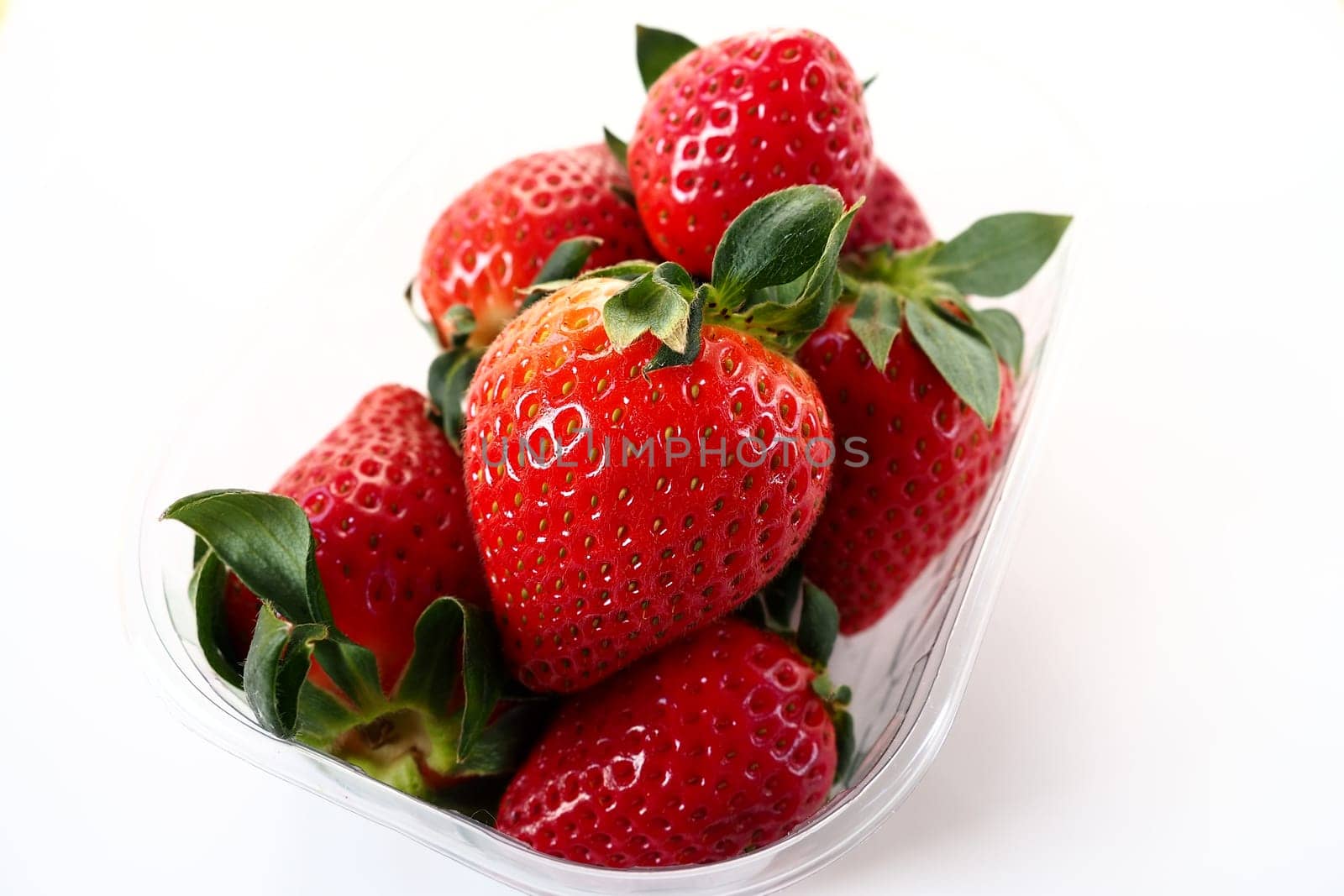 Ripe strawberries in a plastic package on a white background. Delicious fresh berries in a container for sale to customers. Keeping food fresh. Healthy food, vitamins and microelements