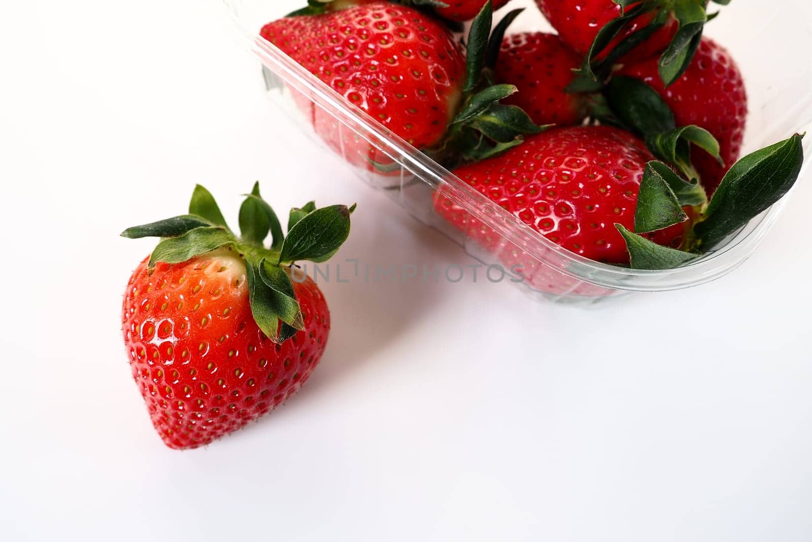 Ripe strawberries in a plastic package on a white background. Delicious fresh berries in a container for sale to customers. Keeping food fresh. Healthy food. One strawberry pulled out of the container