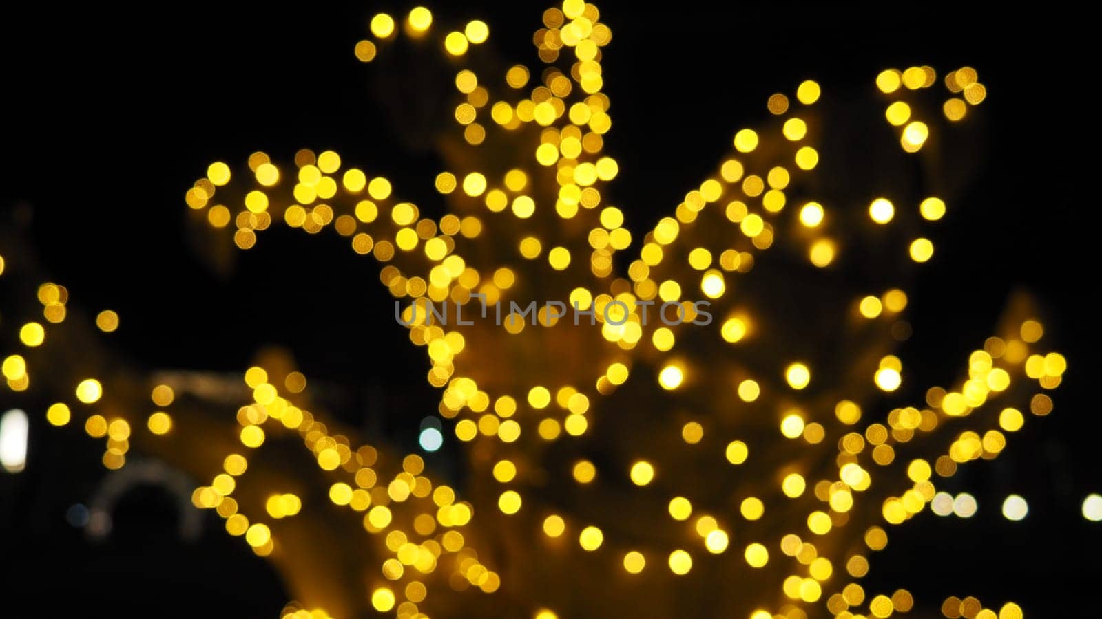 Bokeh on Christmas night. Beautiful round bokeh highlights. Golden and yellow color flashes in the dark. Festive background for New Year Merry Christmas. Blurred defocus. Decoration of city streets