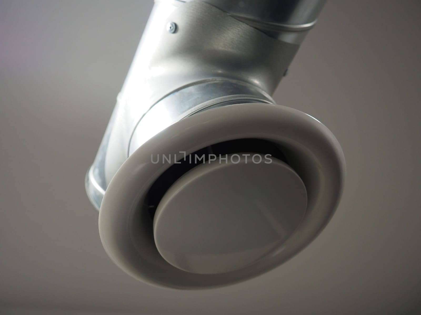 Extractor hood in a public toilet. Round metal pipe with gray air extractor. Engineering ventilation systems. Galvanized pipes under the ceiling of the room. Plastic round tip.