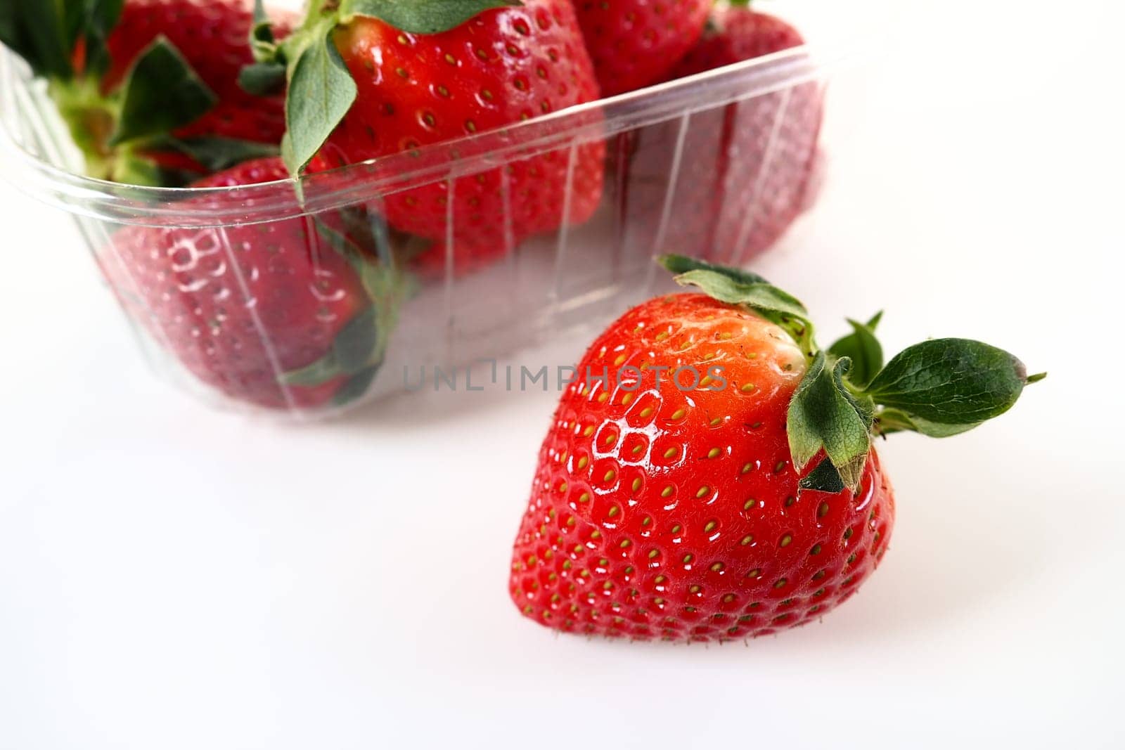 Ripe strawberries in a plastic package on a white background. Delicious fresh berries in a container for sale to customers. Keeping food fresh. Healthy food. One strawberry pulled out of the container