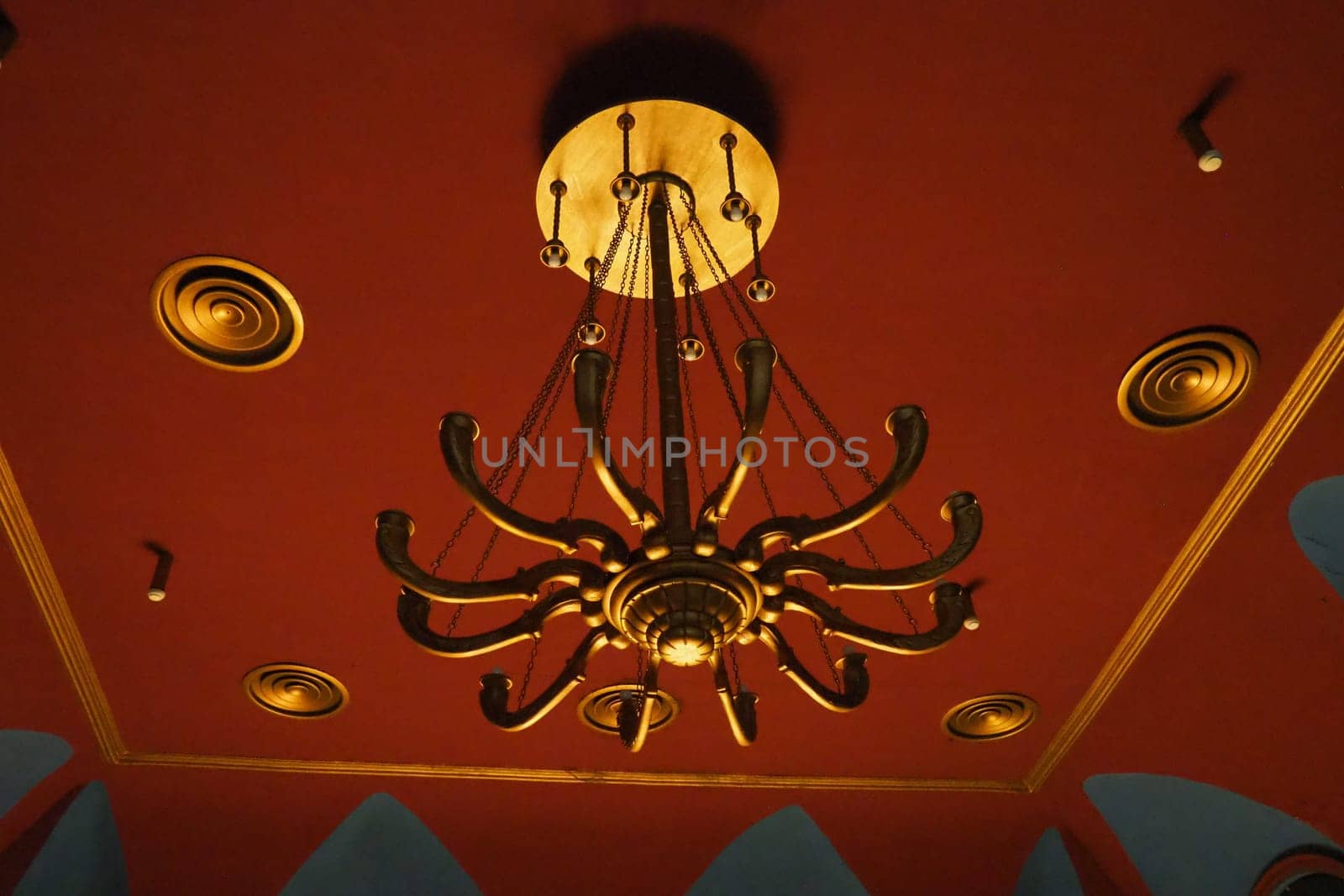 Theatrical golden chandelier under the ceiling of the theater hall. Solemn and rich interior lighting option. Theatrical atmosphere. Interior in red, burgundy and gold. Energy saving and safety