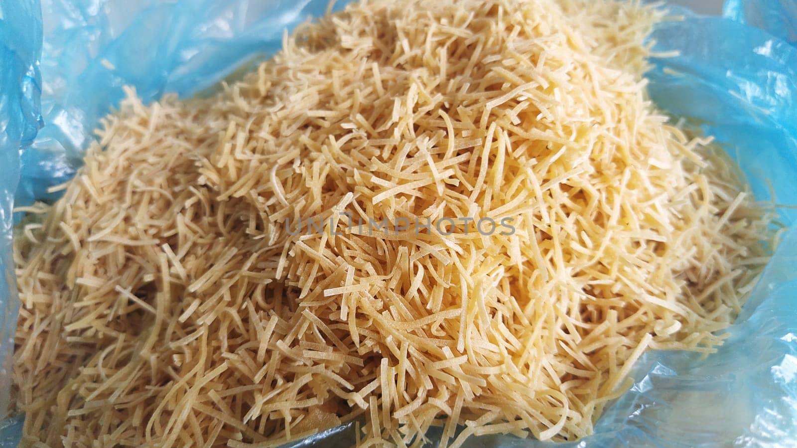 Thin dry vermicelli. Wheat flour product containing gluten, vitamins, carbohydrates, proteins and fats. Small pasta in a blue plastic bag. Fast food.