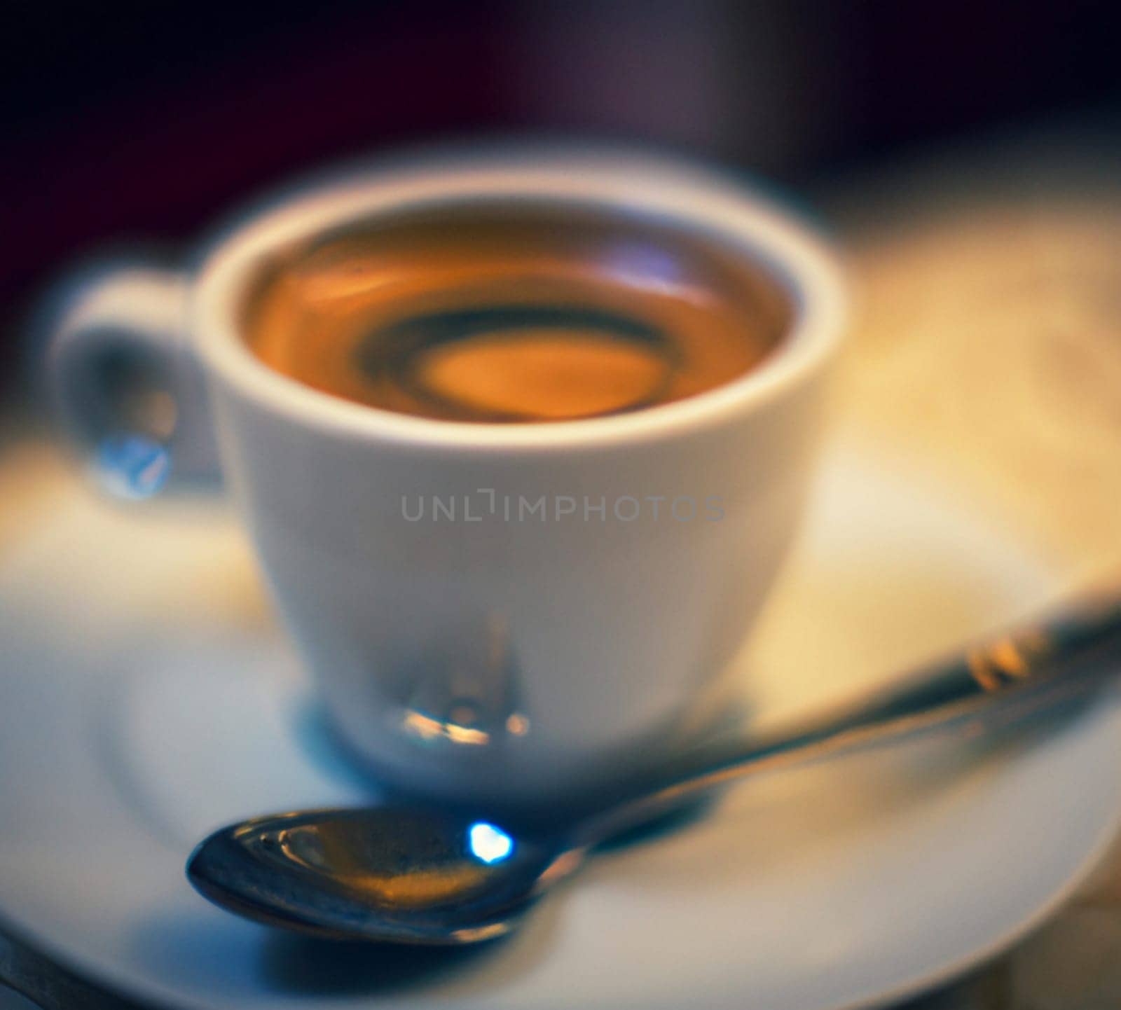 Cup of coffee in cafe. Anamorphic bokeh effect. Tilt-shift photo. Hot coffee in a white cup with a saucer and a spoon. The coffee is getting cold. Aroma of coffee beans. Label or advertisement. Foam