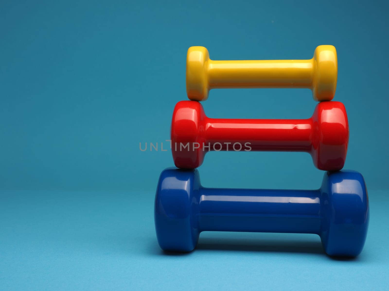 Red, blue and yellow dumbbells on a blue background, space for your text, fitness or diet concept