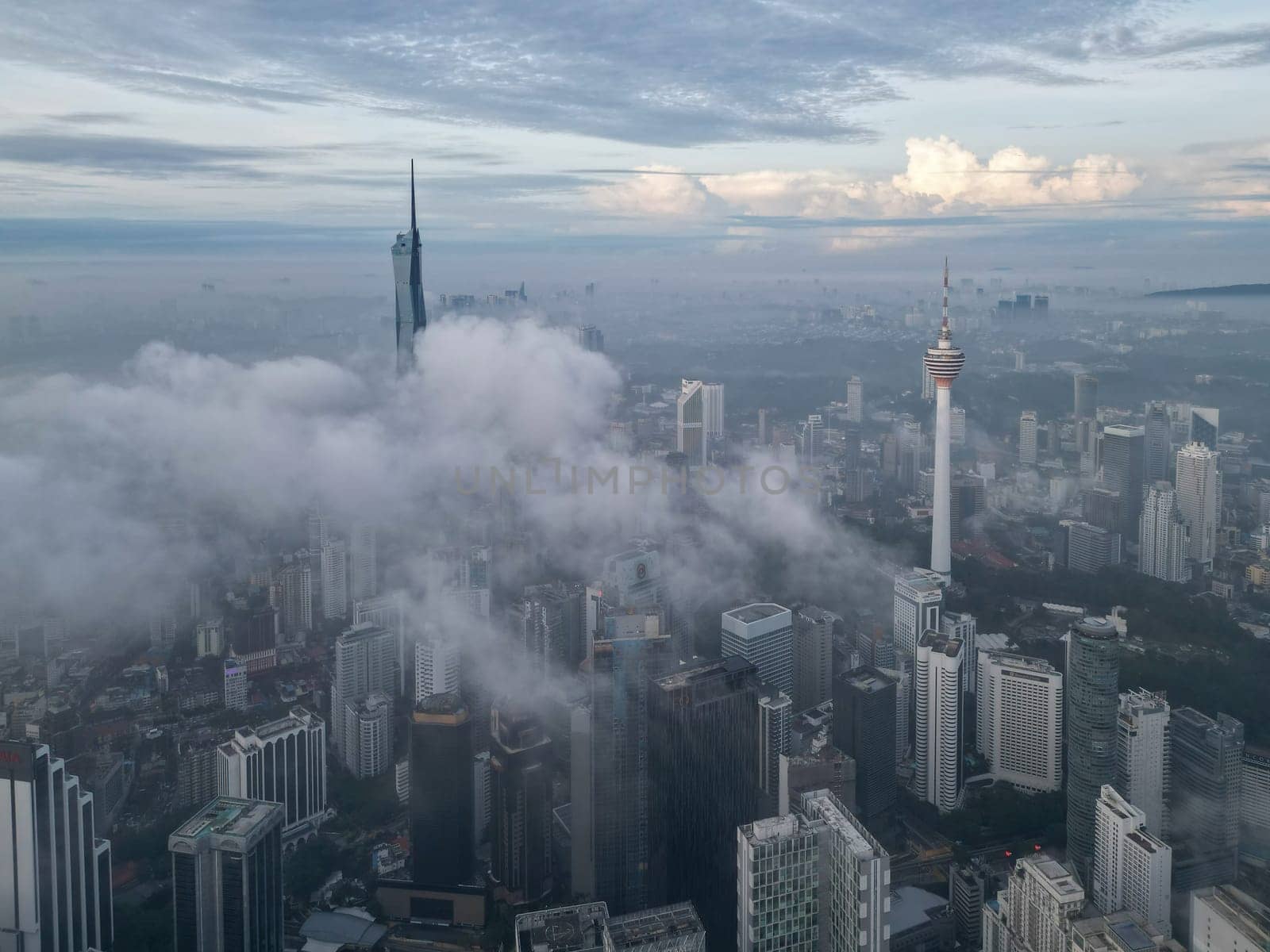 Bukit Bintang, Kuala Lumpur, Malaysia - Nov 13 2022: The tall spire of the Merdeka 118 and KL Tower pierces through the low clouds, creating a surreal view.