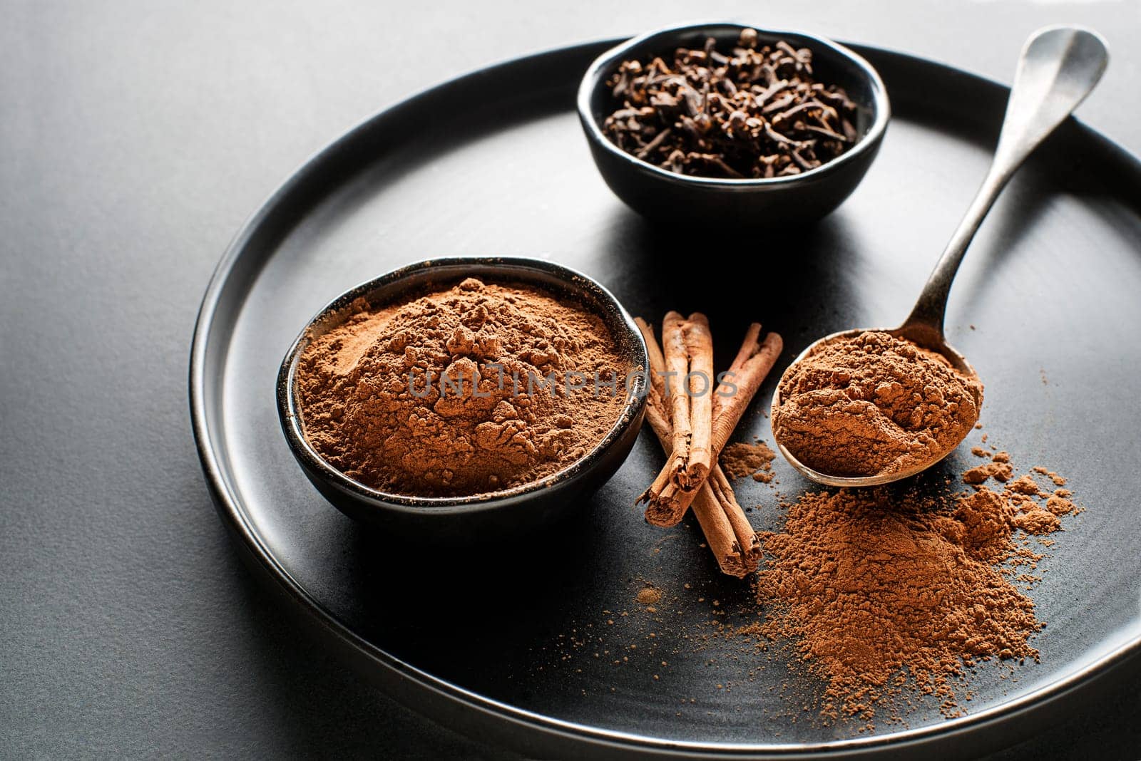 Aromatic cinnamon sticks and cup with cinnamon powder on black background close up