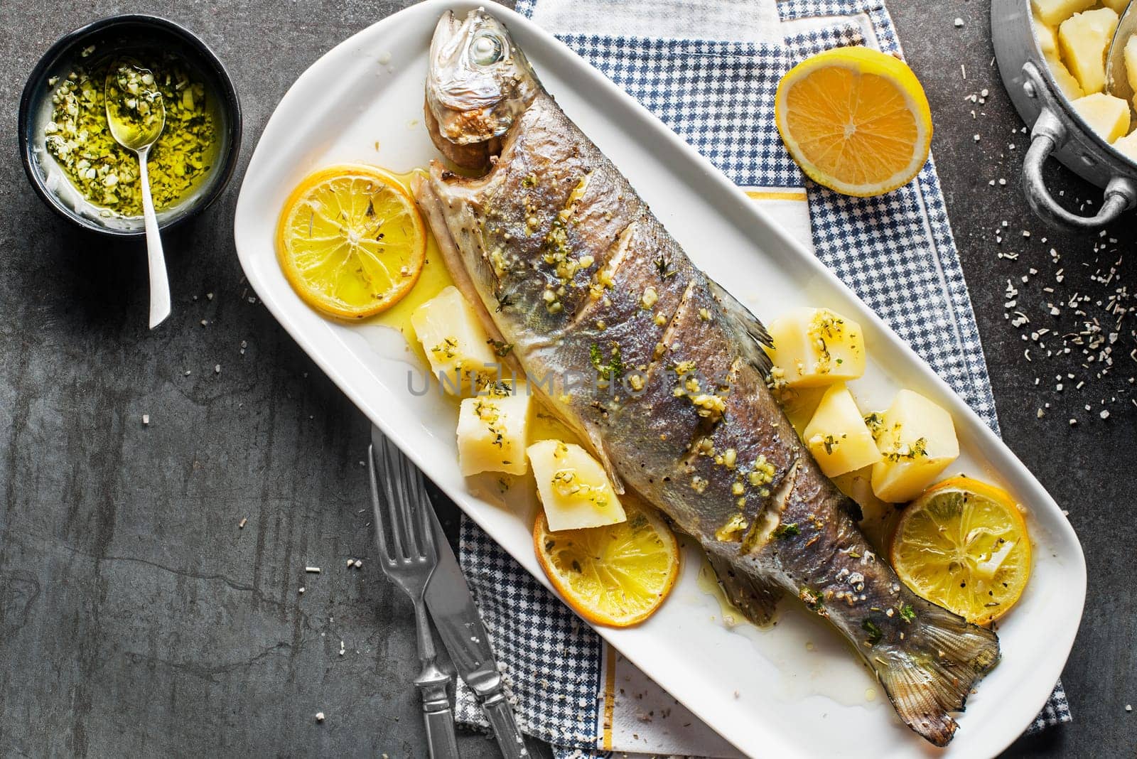 Roasted traditional river trout with salad, potatoes and (garlic, parsley) sauce on grey table background