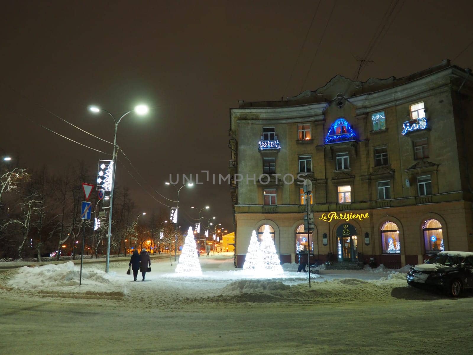 Petrozavodsk, Karelia, Russia, January 01, 2021. Karl Marx Avenue, Cafe Parisianka in the evening in winter. Snow drifts, Christmas street lights and decorations. People walk along the street