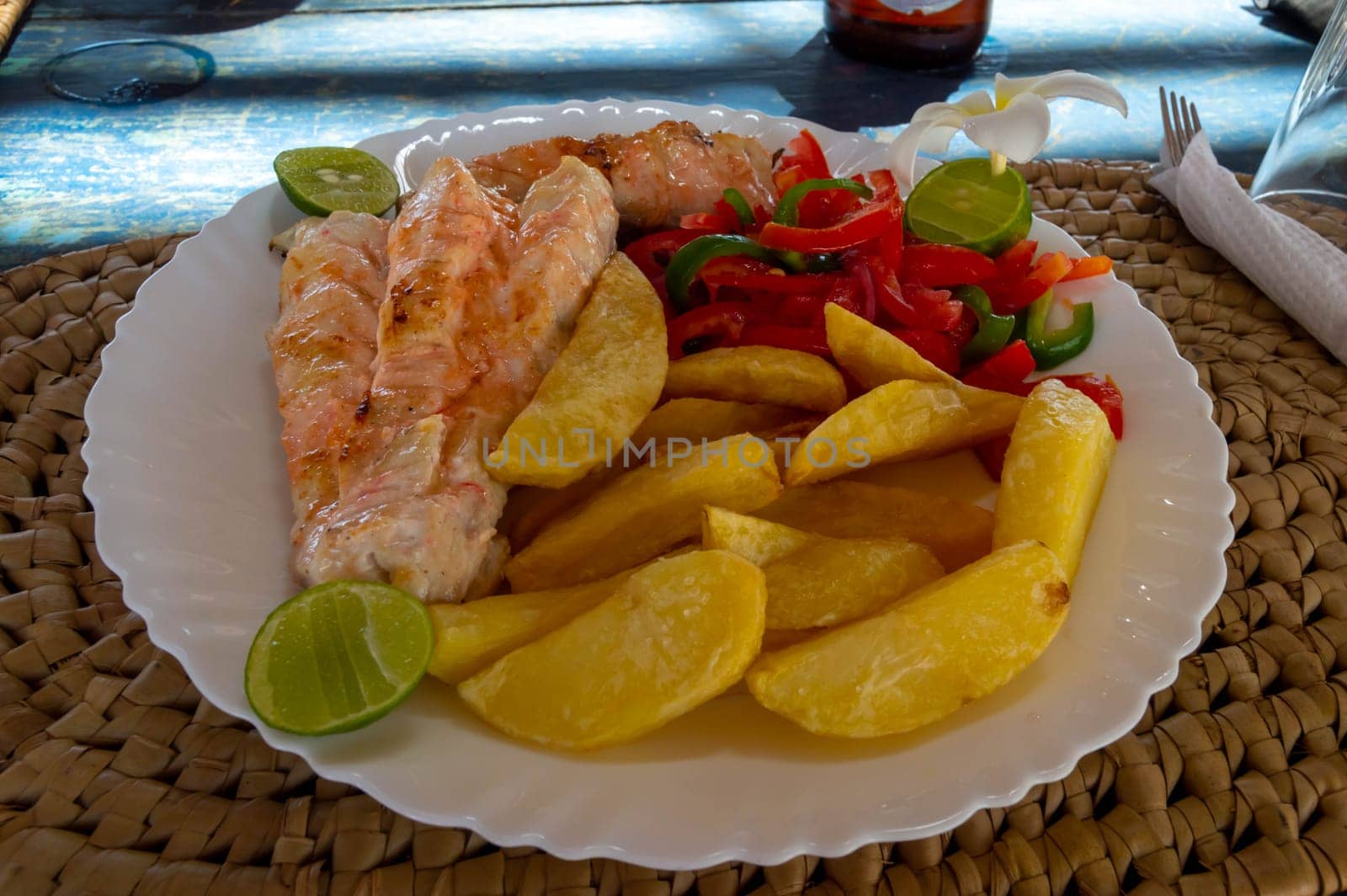 Big dish of fried fish with french fries , sliced peppers and lime served on a white plate