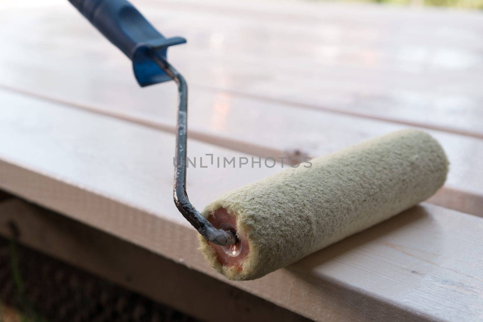 Close up white soft professional paint roller applicator with handle lying on wooden board. Brushing, coloring and making cosmetic repairment. Renewal work, stucco and repair. House remodeling