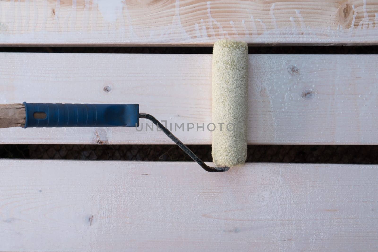 White soft paint roller applicator brush with handle painting wooden fence or floor planks. Cosmetic repair, house renovation, creative occupation. Brushing, making cosmetic repairment. Top view