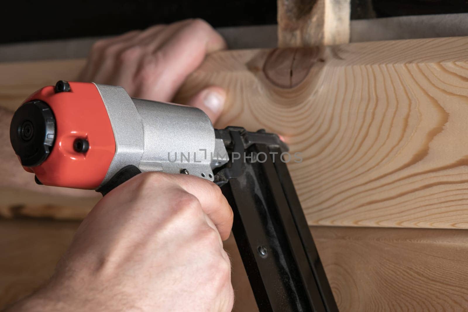 Close up cropped carpenter male hands using pneumatic nailer, stapler gun for wooden timber plank. Making layout on wooden plank. Builder handwork and wood repair technology. Craftsmanship, handcraft