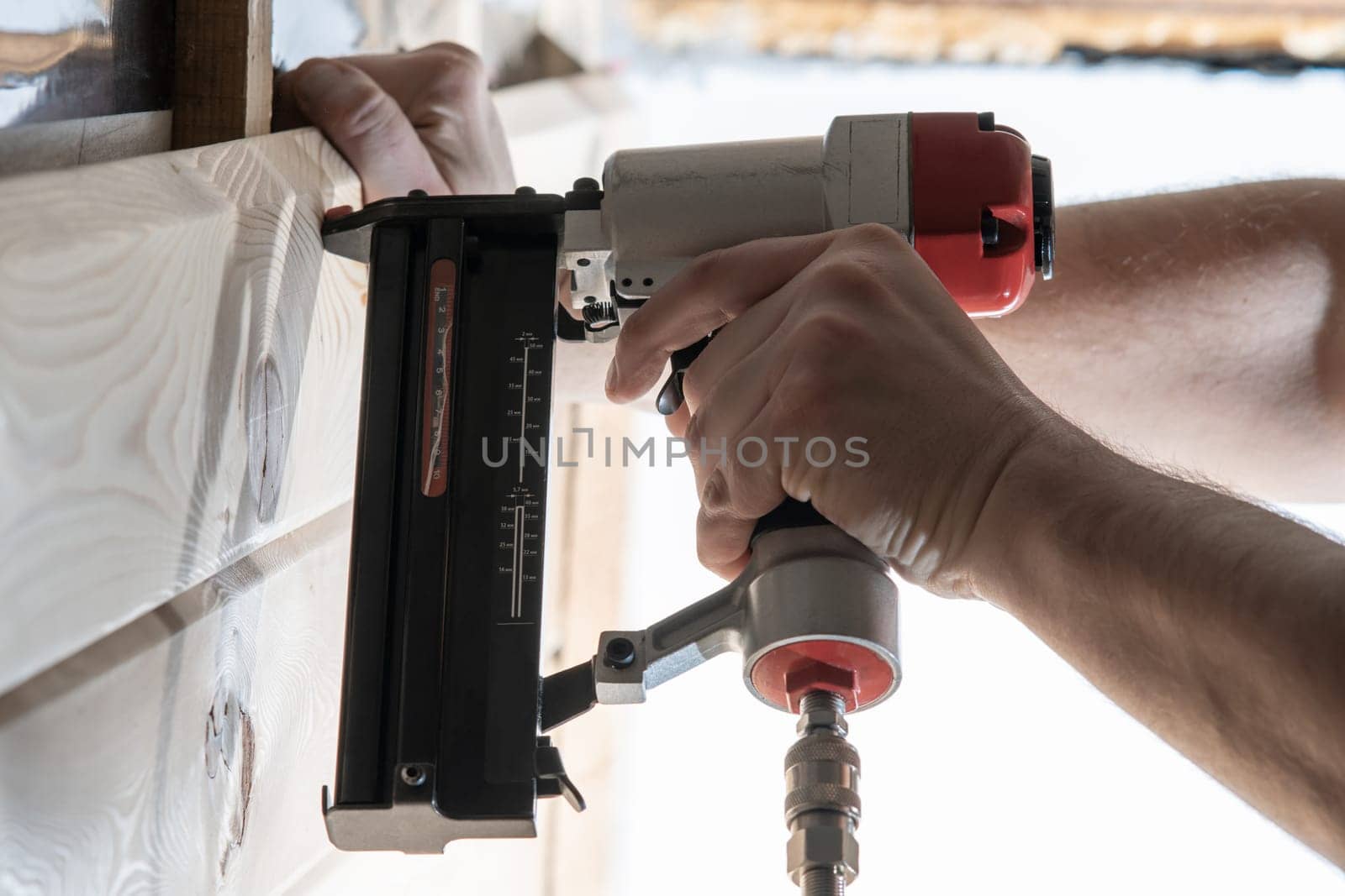 Cropped male builder hands use pneumatic stapler gun for clipping wooden timber board. Scoring metal nails and staples, making layout on wooden plank. Builder and civil engineer occupation. Side view