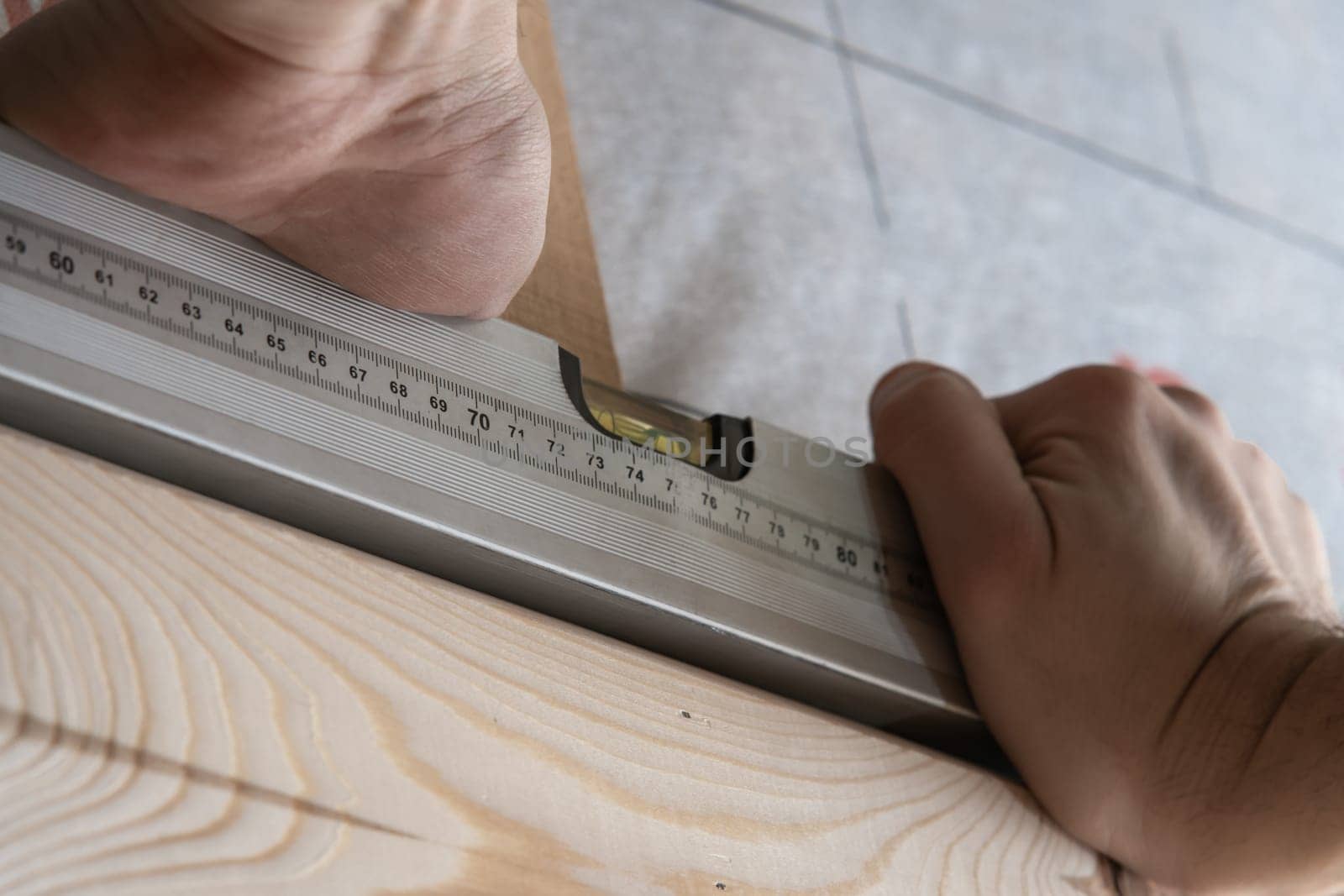 Close up cropped male worker hands hold water pass level for building wooden structure. Renovation and repair of houses. Measuring and fixing level, builder equipment for carpenters. Low angle view
