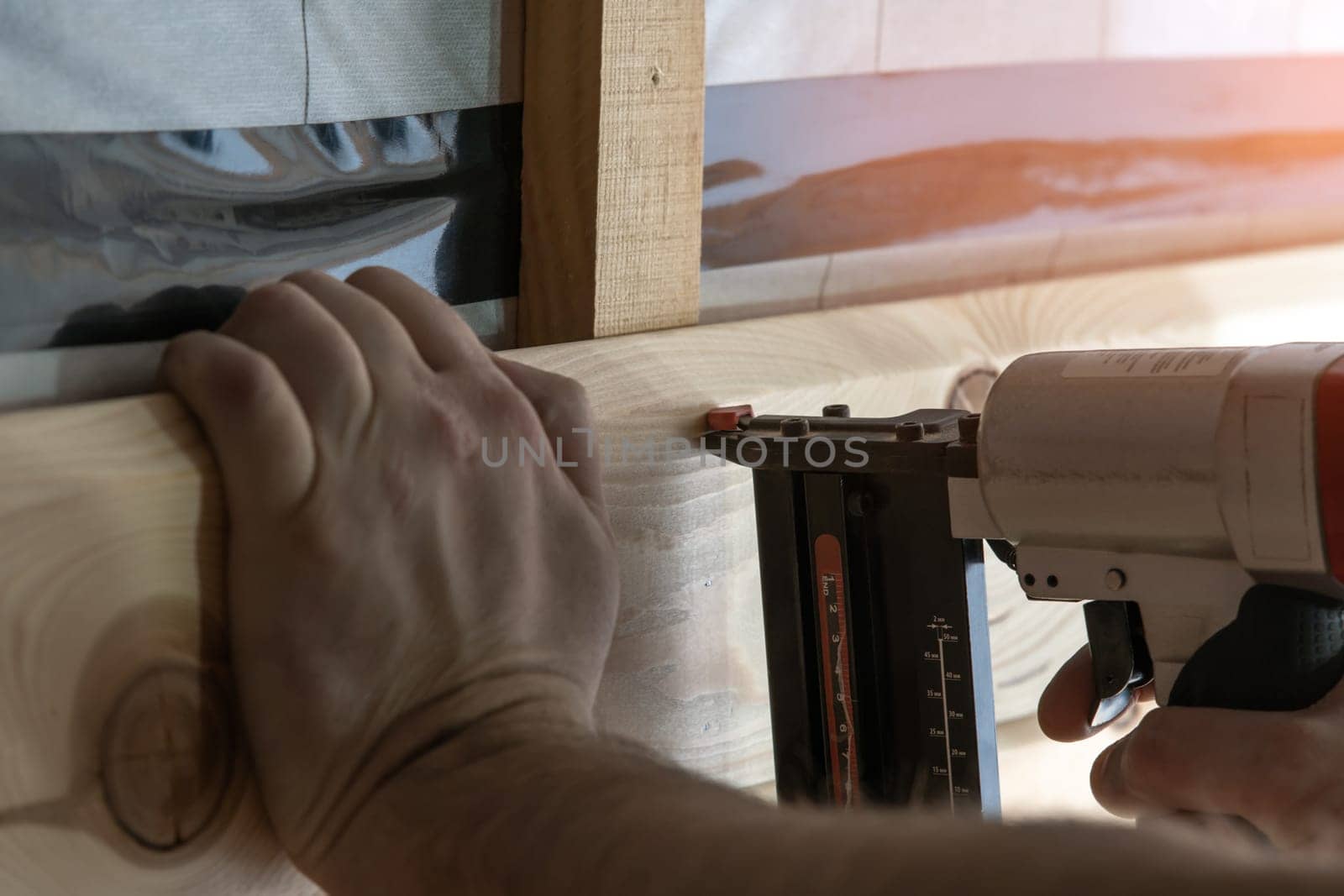 Cropped builder hands holding pneumatic nail gun, stapler for wooden board. Scoring and setting up metal staples, making layout on wooden plank. Handyman work, do it yourself. Builder occupation