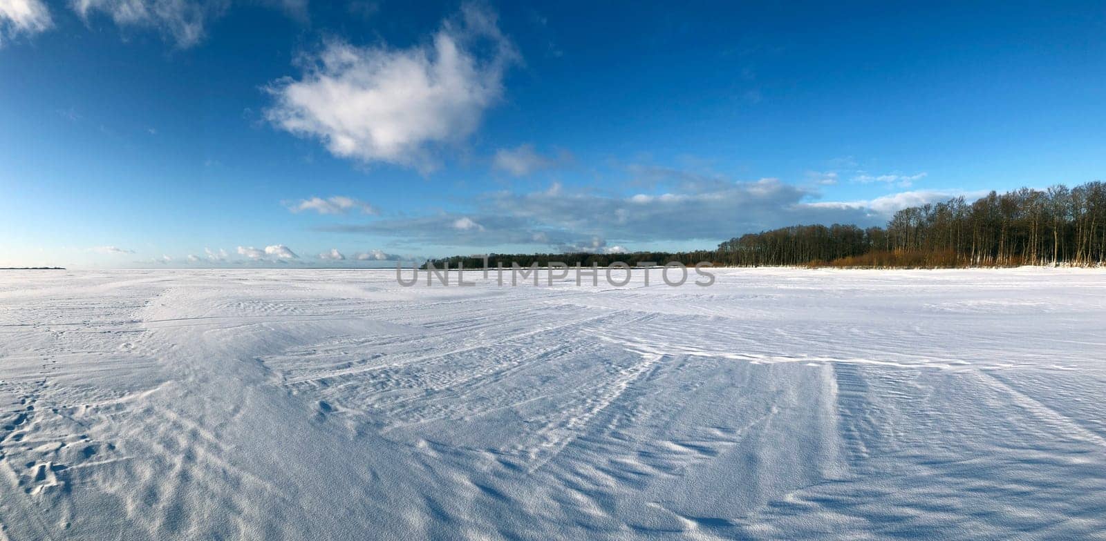 winter panorama, frozen endless expanse of the lake, white snow with traces, blue sky, clear frosty air, sunny day