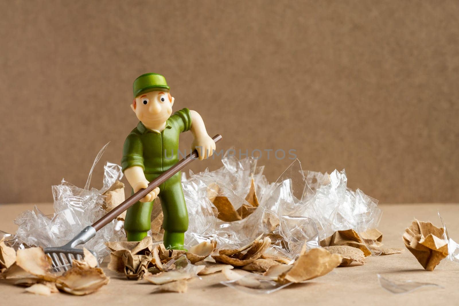 A toy man in a worker's suit rakes a large amount of garbage. Environmental protection and ecology concept
