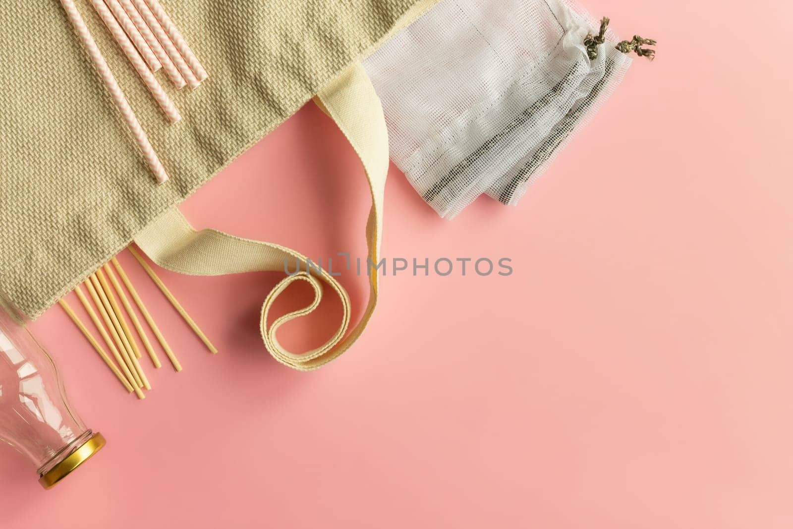 Fabric cotton shopping bags, glass bottles and jars, paper straws and wooden sticks on a pink background. Zero waste and ecological concept. Top view. Copy space.