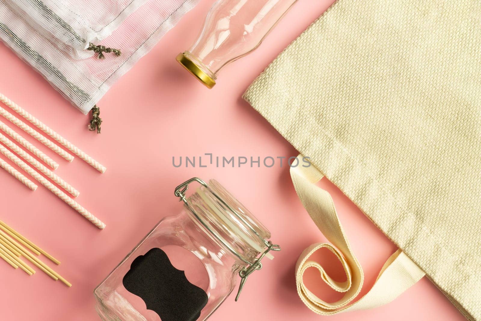Fabric cotton shopping bags, glass bottles and jars, paper straws and wooden sticks on a pink background. Zero waste and ecological concept. Top view. Copy space.