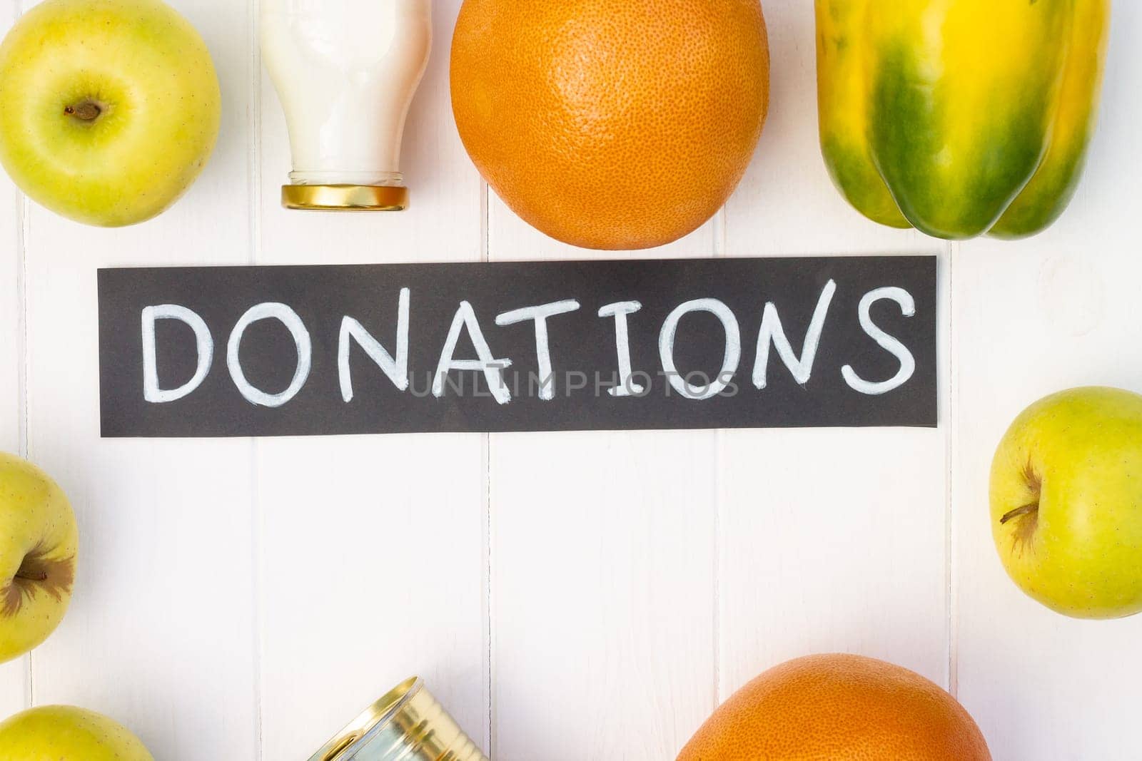 Cereals, canned food, milk, vegetables and fruits with a chalk Donations sign on a white wooden table. Flat lay. Copy space. Charity and donation concept.