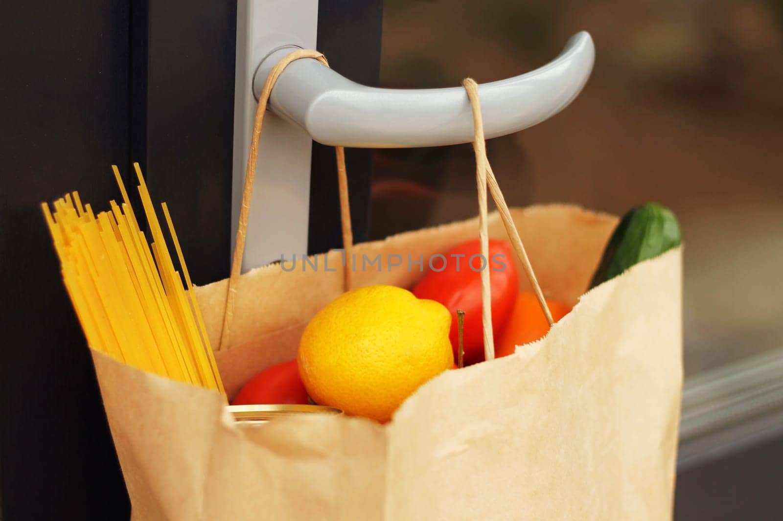 A paper bag with food from delivery on the handle of the front door, closeup. Contactless delivery. Donation during coronavirus. Volunteering and delivery during quarantine concept.