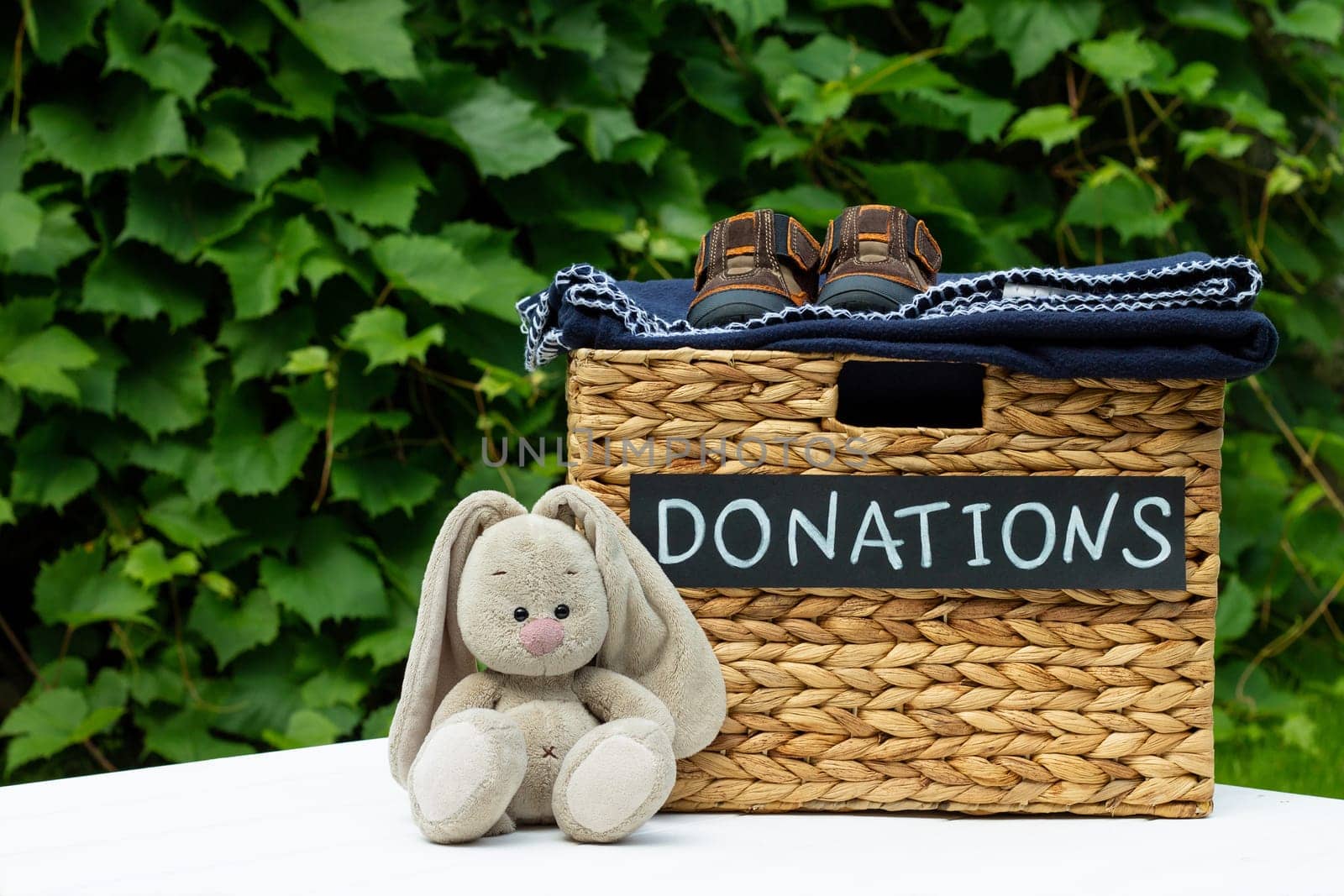 Donation box for clothing donations with children shoes and toy hare on a greenery background. Charity and donation concept. Copy space.