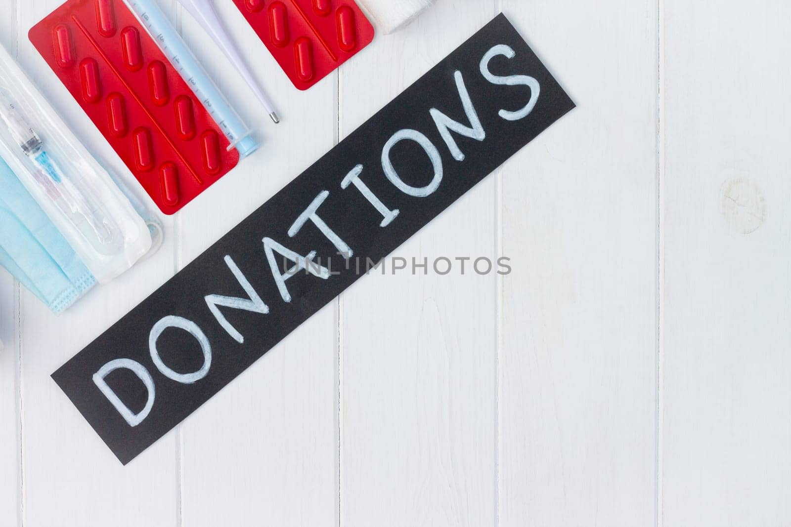 Medications, masks, gloves, syringes, thermometer with a chalk Donations sign on a white wooden table. Flat lay. Copy space. Charity and donation concept.
