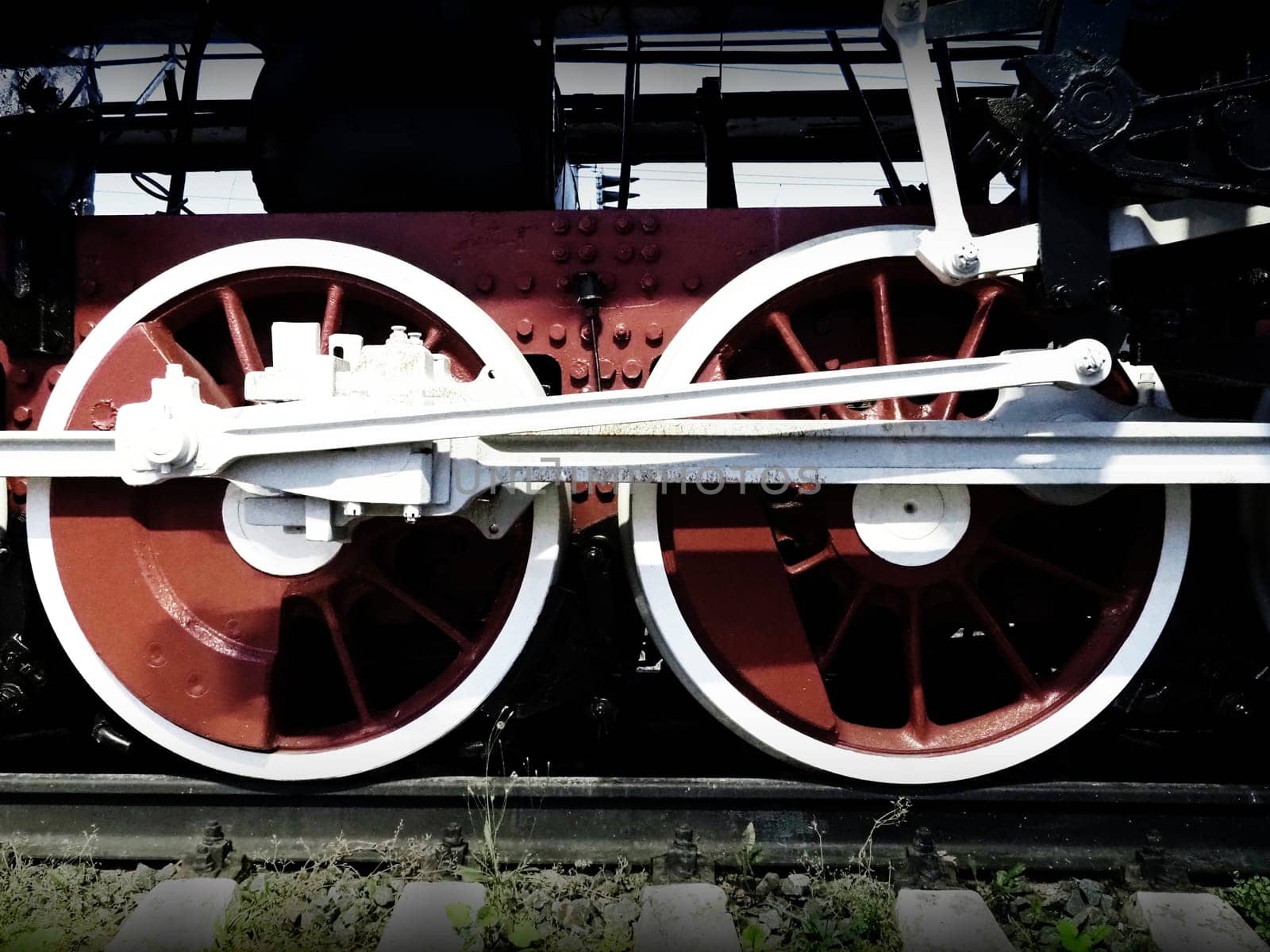 Retro vintage wheels of a locomotive or train close up. Red large heavy metal wheels with piston guiding mechanisms. Locomotive of the 19th - 20th centuries with a steam engine. Bright vivid photo.
