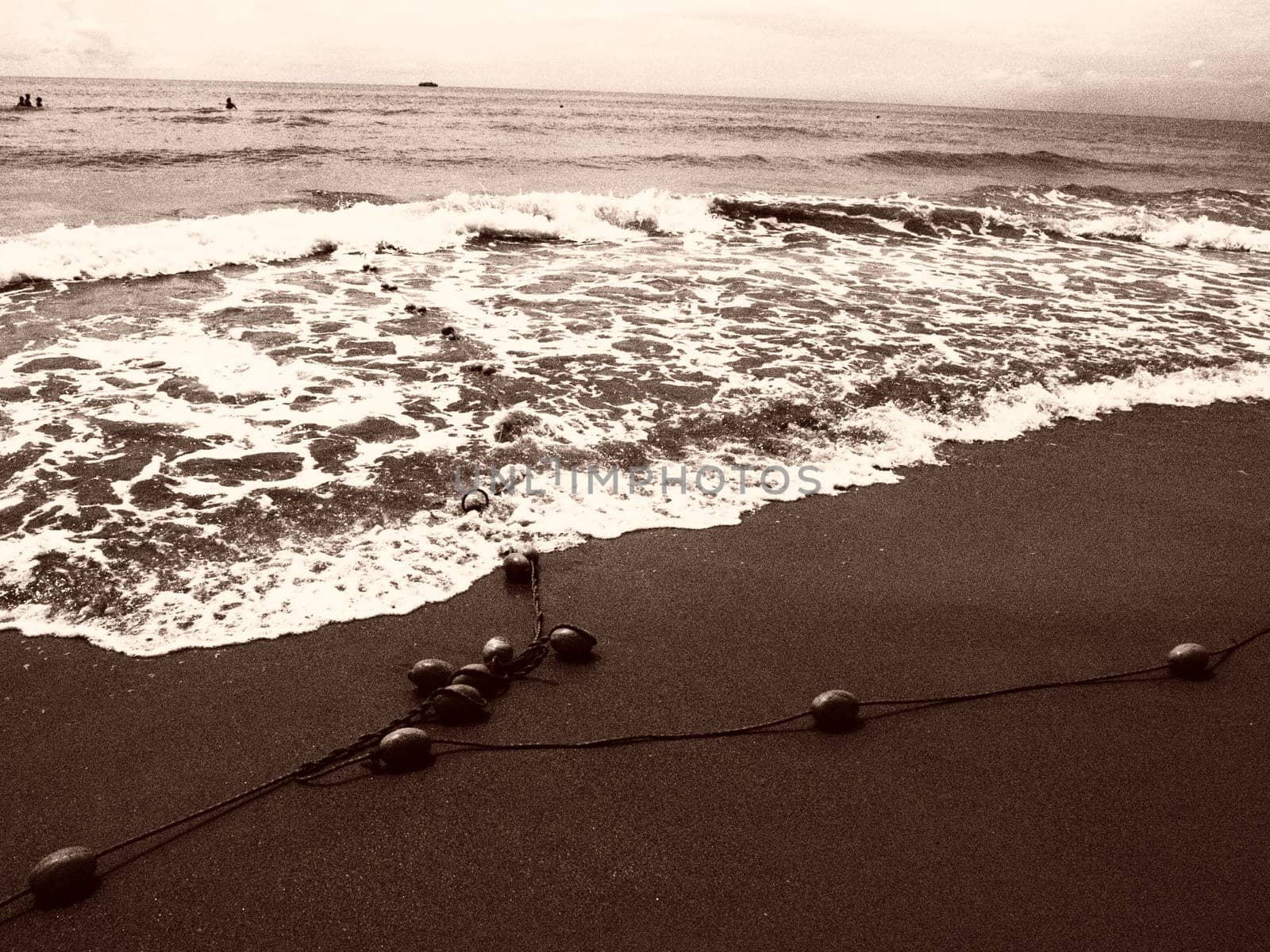 Buoys on a rope near sea water. The buoys are bright pink restraints to alert people to the depth of the water. Sepia. Delimiting a place on a sandy beach between hotels. Waves with bubbles.