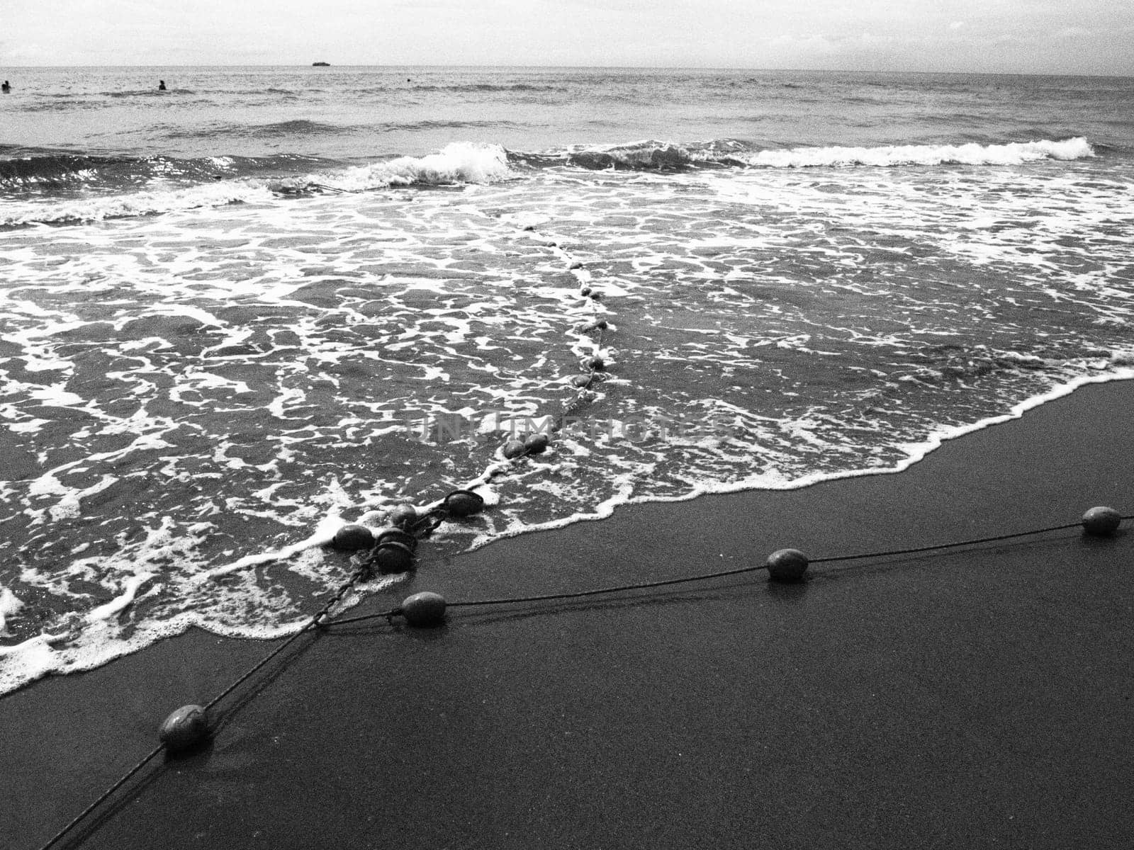 Buoys on a rope near sea water. The lifebuoys restraints to alert people to the depth of the water. Delimiting a place on a sandy beach between hotels. Wave with bubbles. Black white photo monochrome.