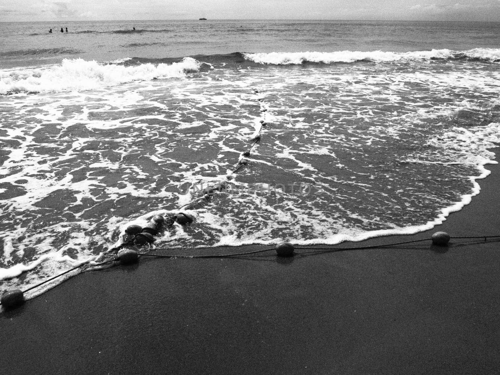 Buoys on a rope near sea water. The lifebuoys restraints to alert people to the depth of the water. Delimiting a place on a sandy beach between hotels. Wave with bubbles. Black white photo monochrome.