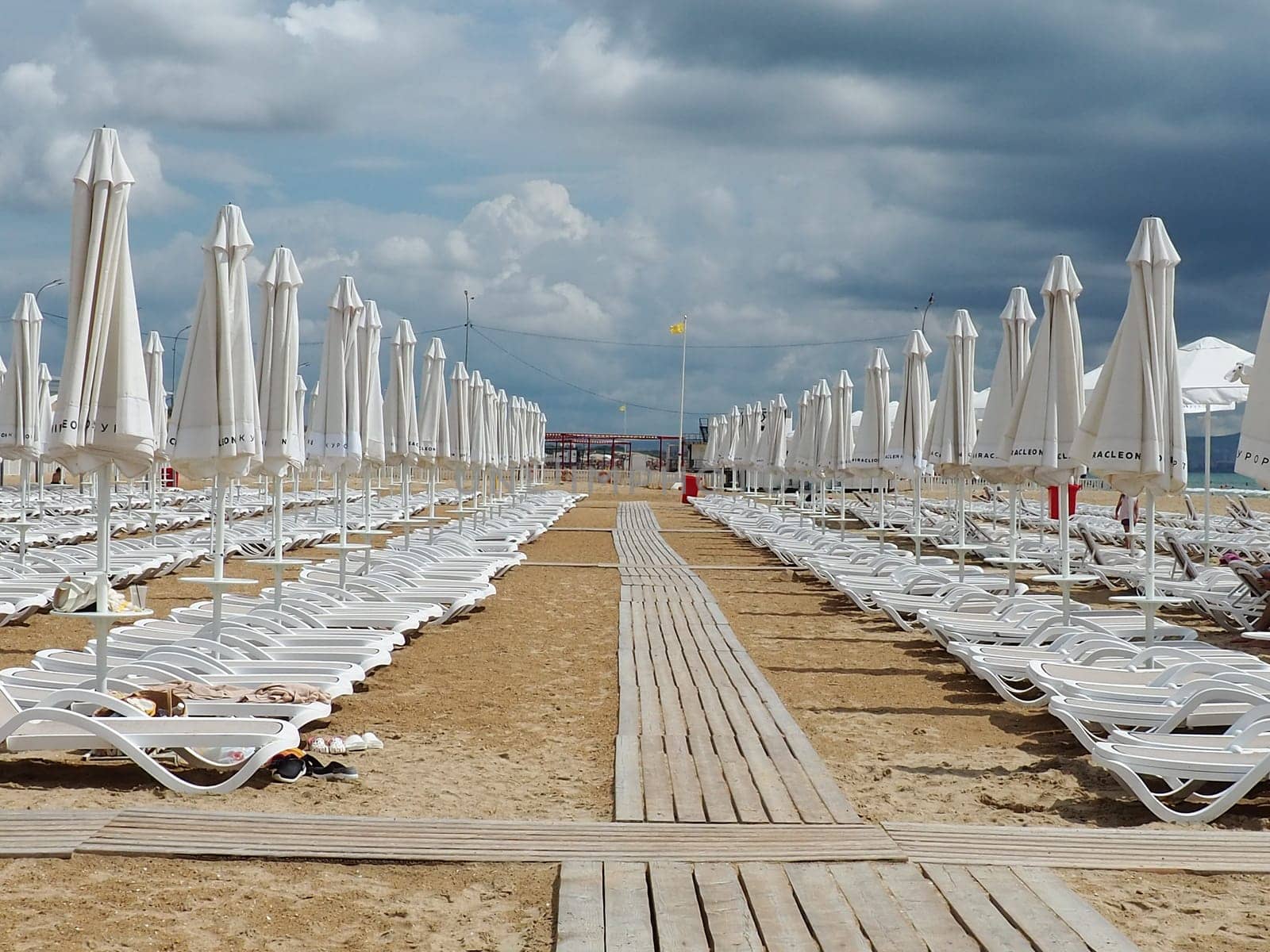 Wet sunbeds and umbrellas on the sea beach during heavy rain storm. Rolled up parasol on the beach against dark cloudy sky. Invasion of a typhoon, cyclone or storm on the sea or ocean. Beach season
