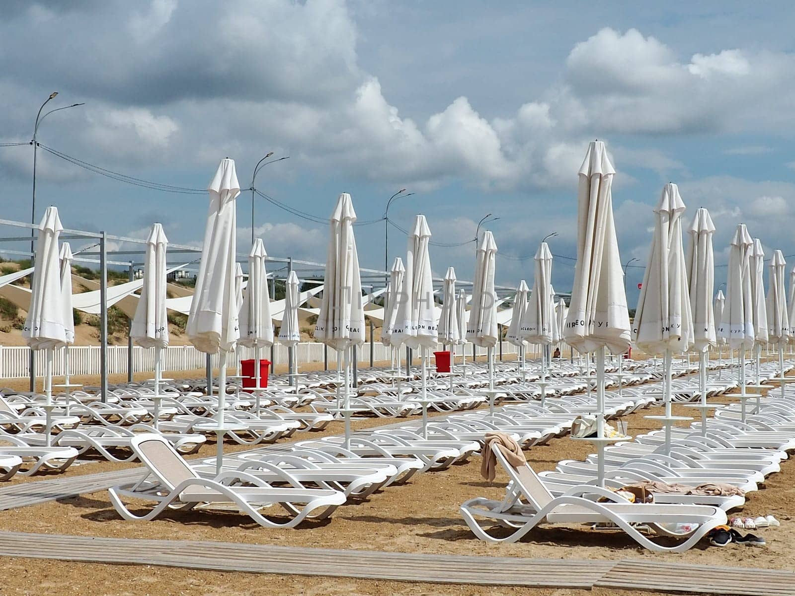 Wet sunbeds and umbrellas on the sea beach during heavy rain storm. Rolled up parasol on the beach against dark cloudy sky. Invasion of a typhoon, cyclone or storm on the sea or ocean. Beach season