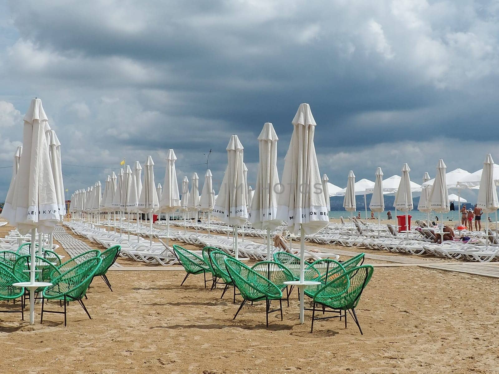 Anapa, Russia, August 15, 2021 Sun loungers and umbrellas on the sandy sea beach after the rain. Beach season. Beach cafe with wicker chairs. Tourists walking people. A storm warning. Cumulus clouds.