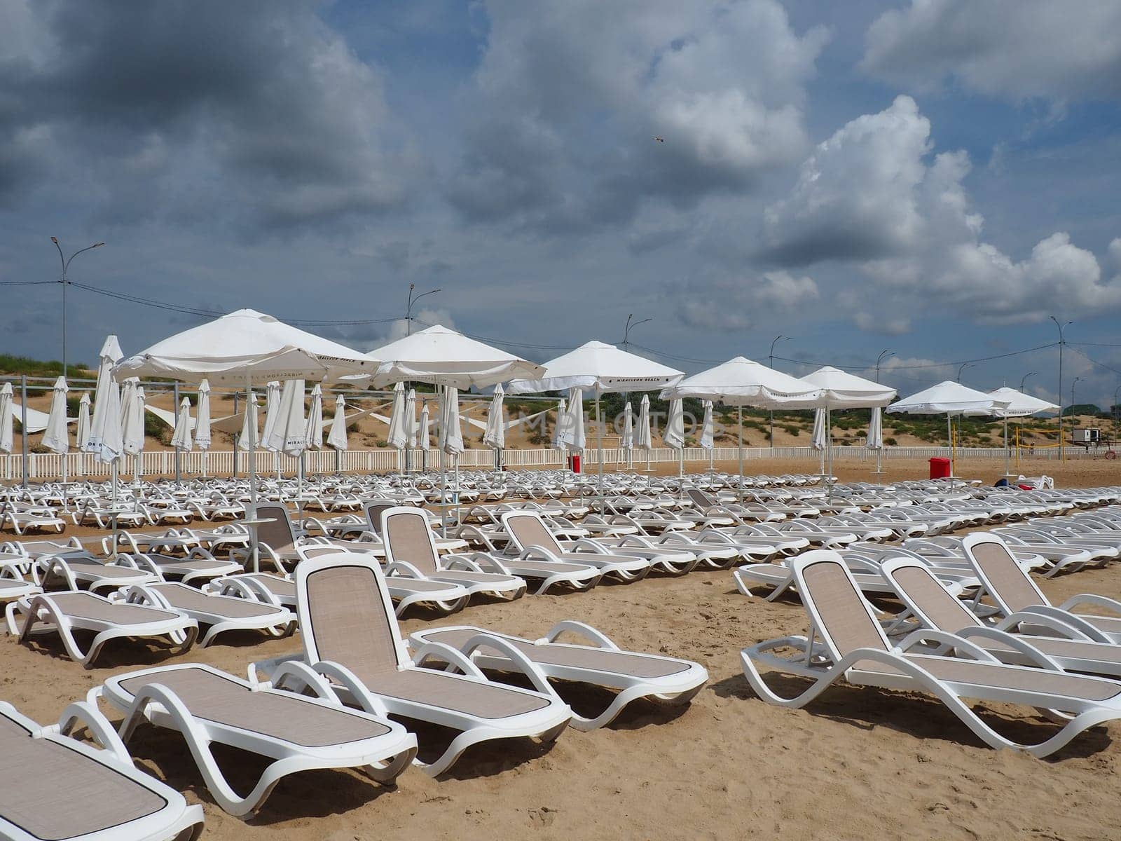 Anapa, Russia, August 15, 2021 Wet sunbeds and umbrellas on the sea beach during heavy rain storm. Rolled up parasol on the beach against dark cloudy sky. Invasion of a typhoon, cyclone or storm.