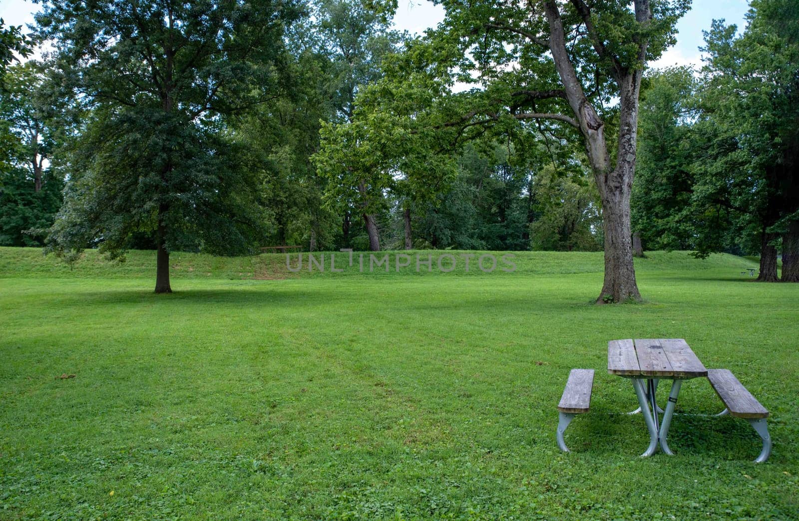 An empty picnic table by the exterior of the Great Circle at the Newark Earthworks built by prehistoric indigenous people in Ohio. Green grass, sunny outdoors with no people and copy space.