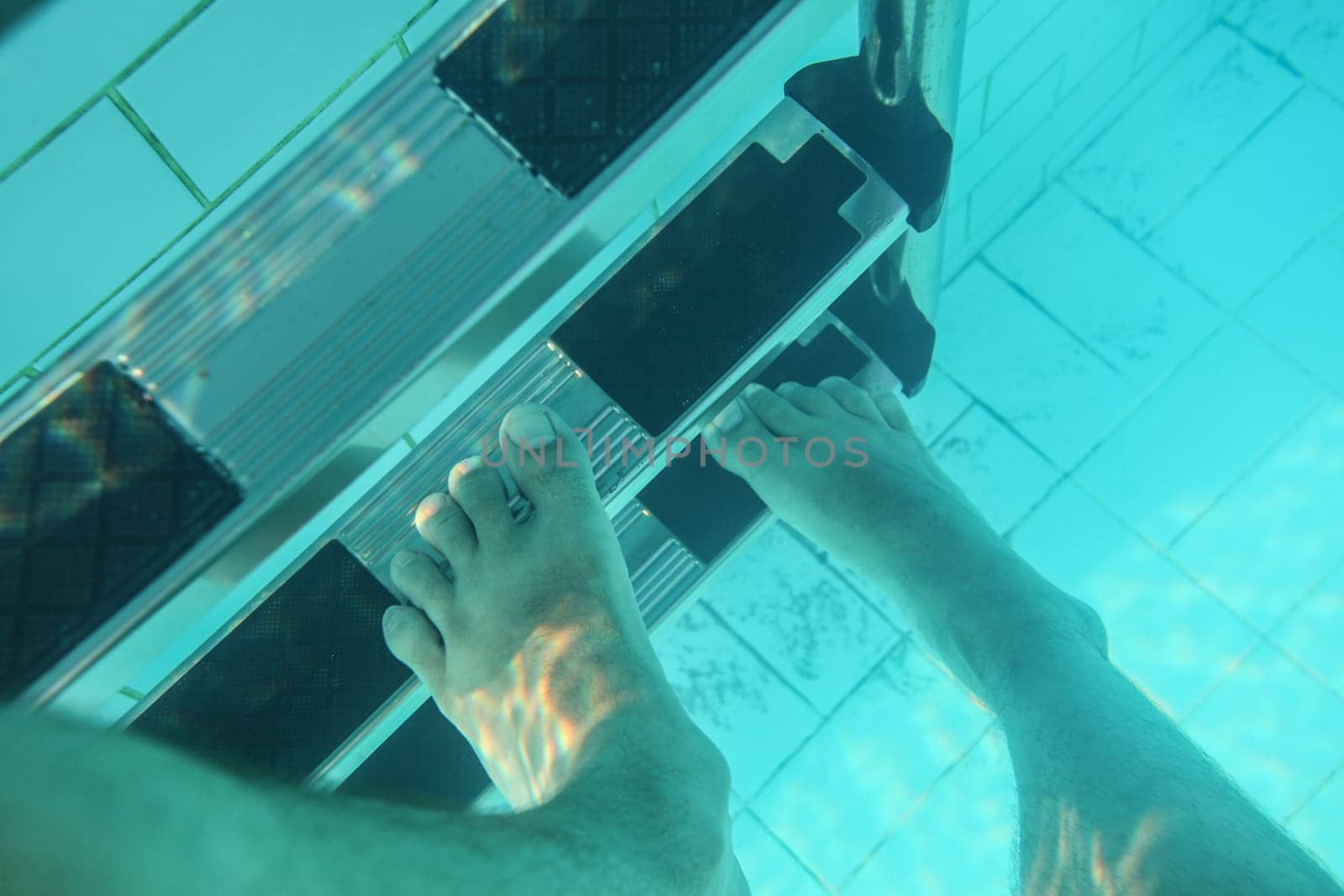 Underwater photo, man feet stepping on pool stairs.