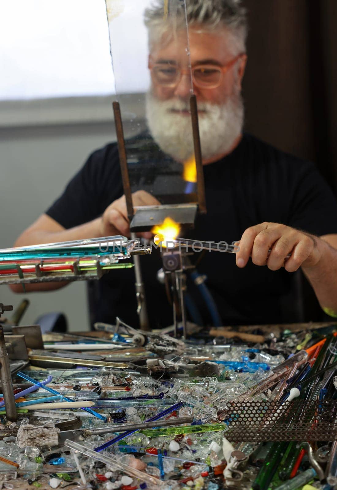 Venice, Italy - September 5, 2022: Glassworker while shaping the glass with a very high temperature flame in its artisan workshop in Venice. Italy