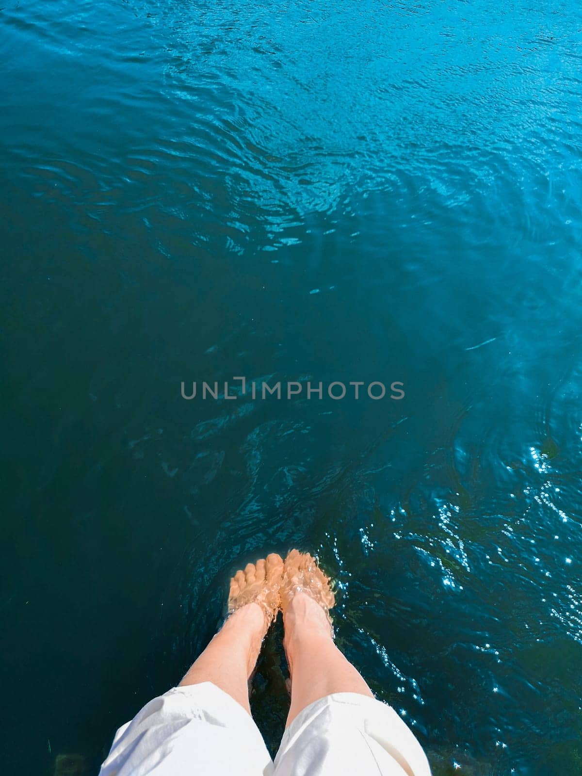 A woman lowered her feet into turquoise seawater.