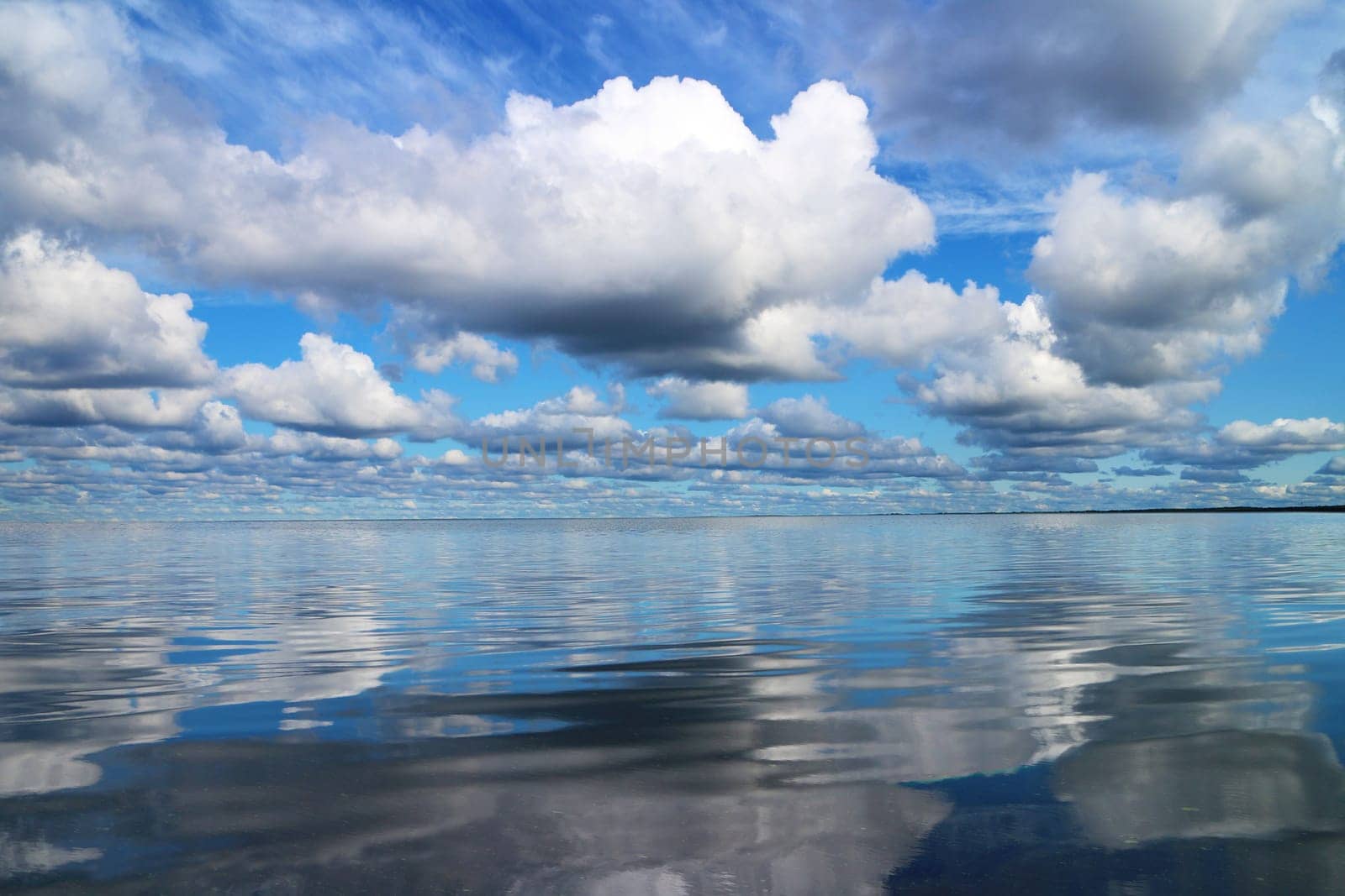 beautiful seascape, cumulus clouds in the blue sky are reflected in the smooth water