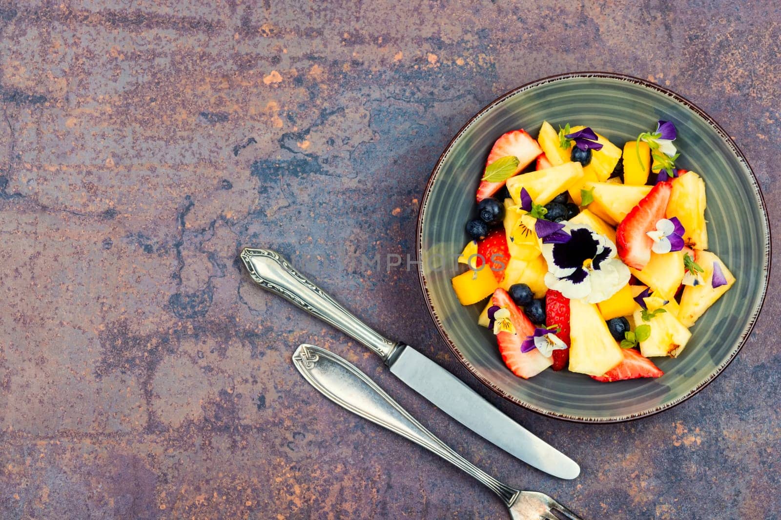Salad of pineapple, strawberries and berries, decorated with edible flowers. Clean ealthy eating