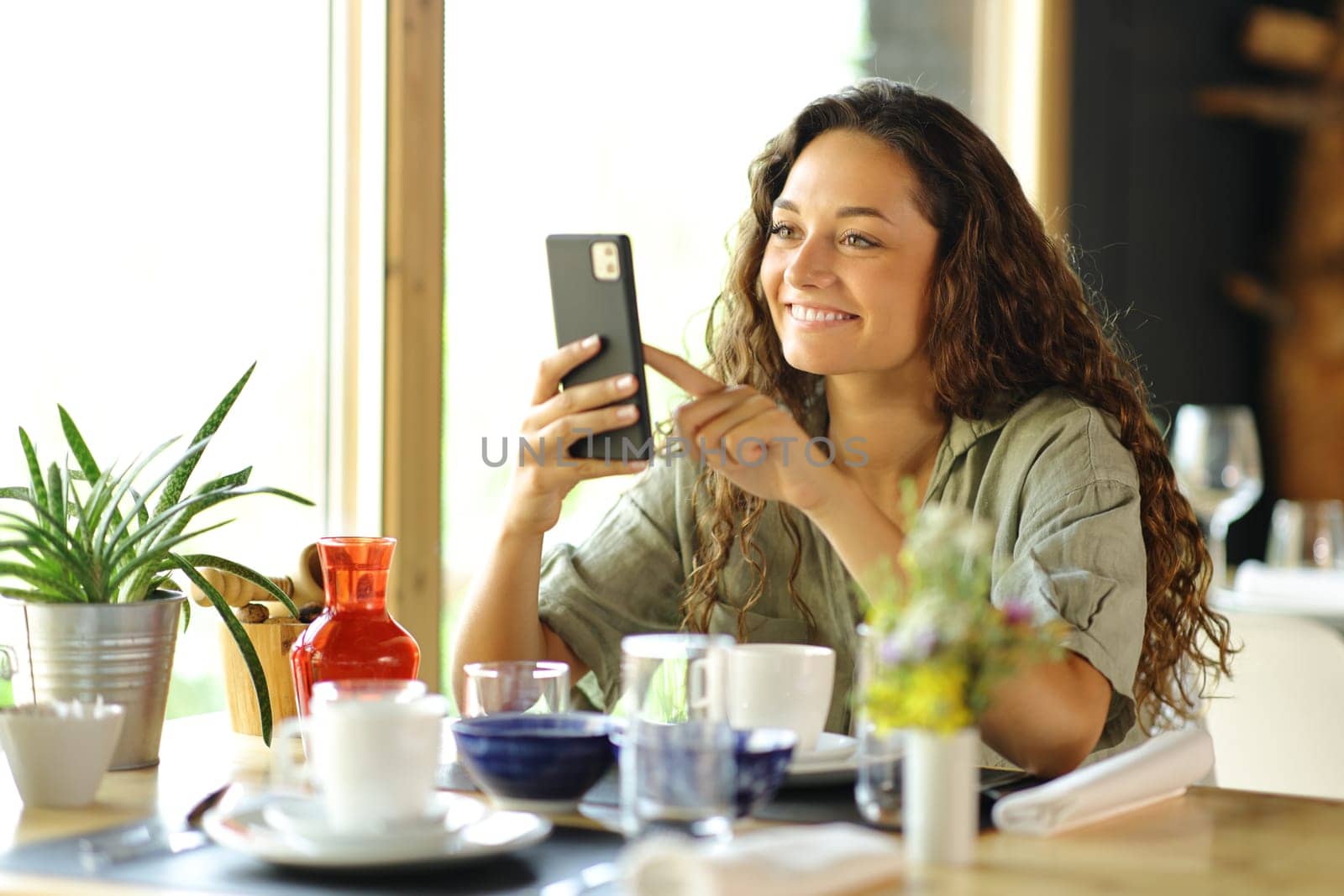 Happy woman checks smart phone at breakfast in a restaurant