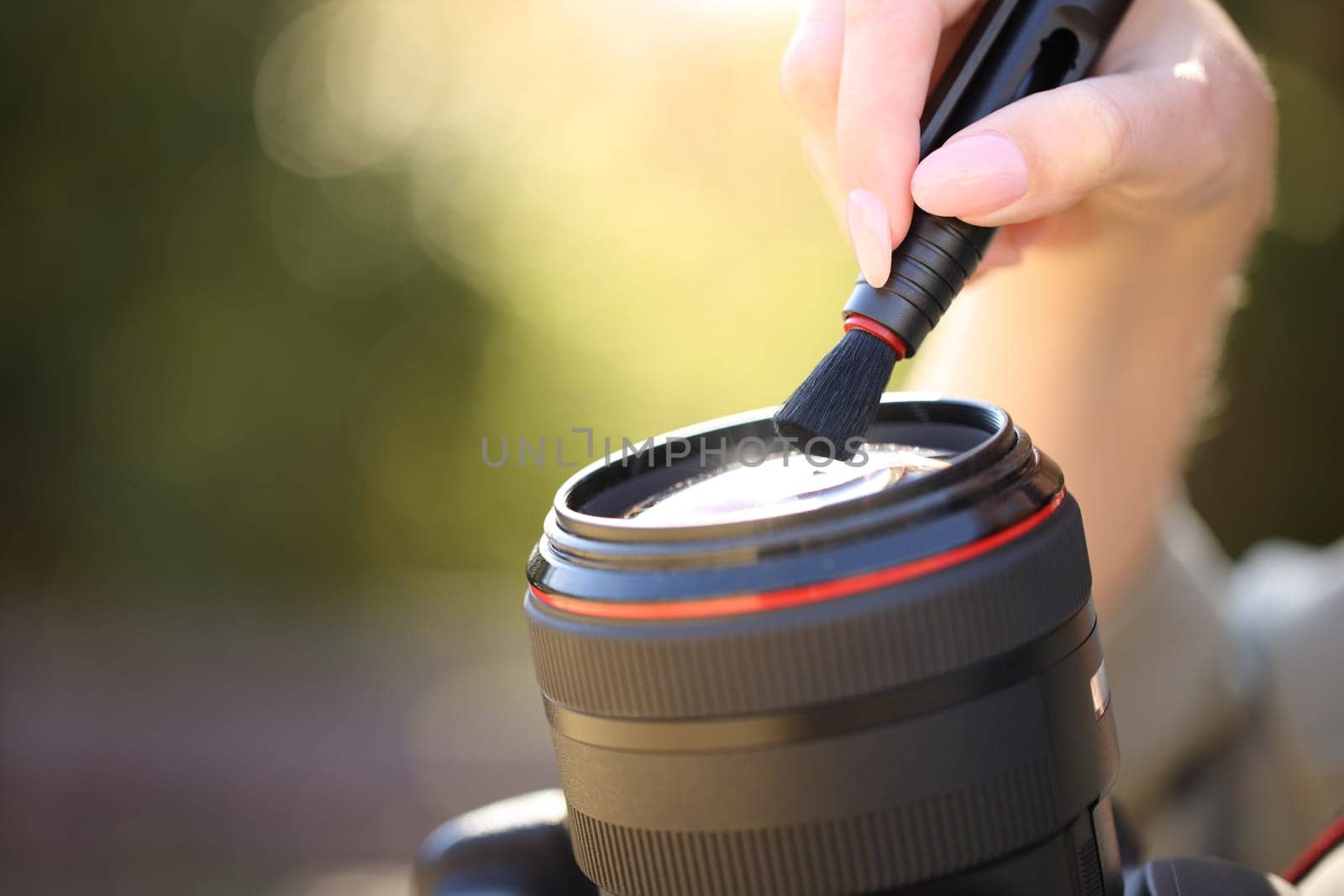 Close up portrait of a photographer cleaning camera lens with brush outdoors
