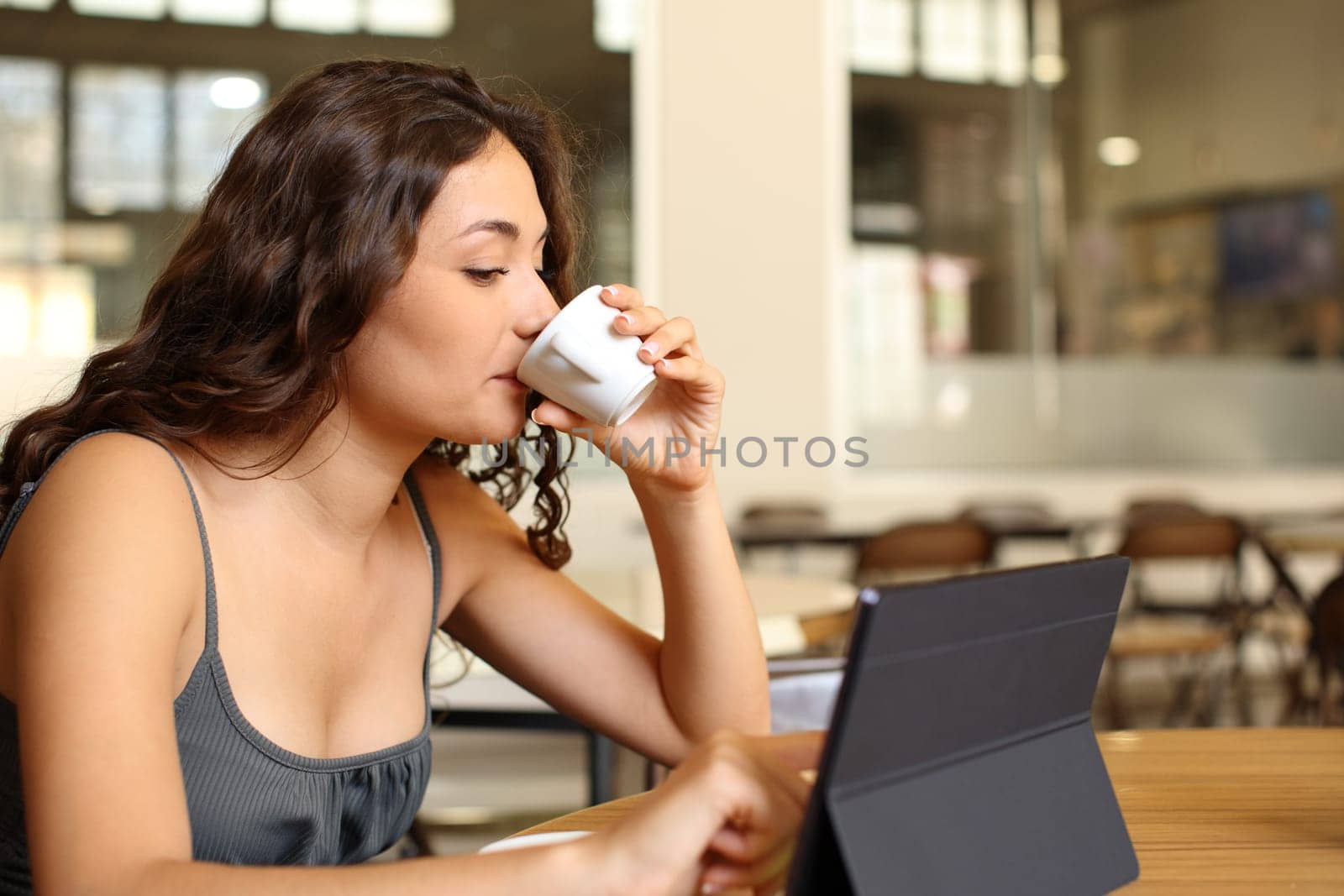 Woman drinking coffee and using tablet in a restaurant