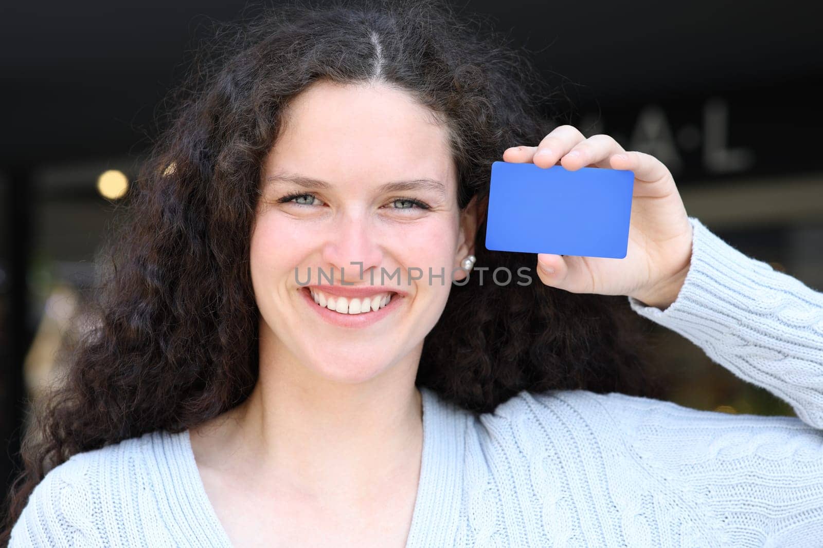 Front view portrait of a woman showing blank blue credit card in the street