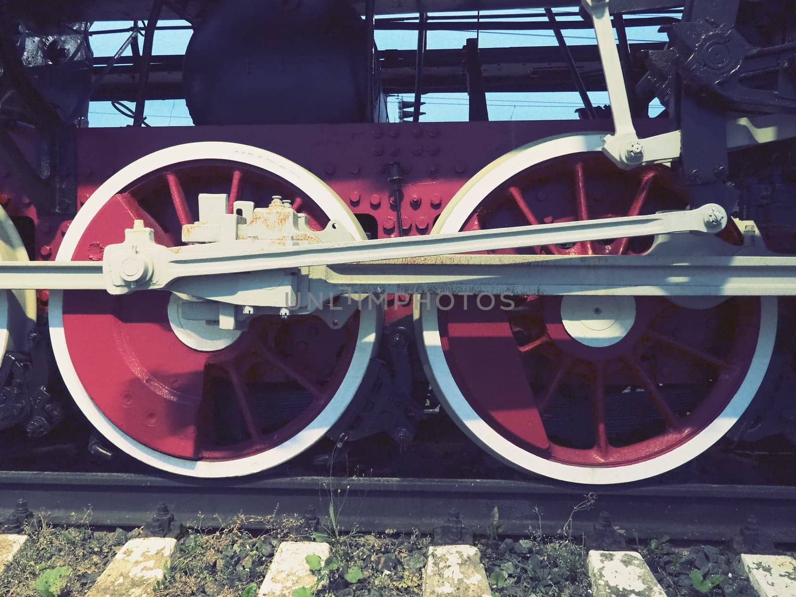 Retro vintage wheels of a locomotive or train close up. Red large heavy metal wheels with piston guiding mechanisms. Locomotive of the 19th - 20th centuries with a steam engine. Retro style