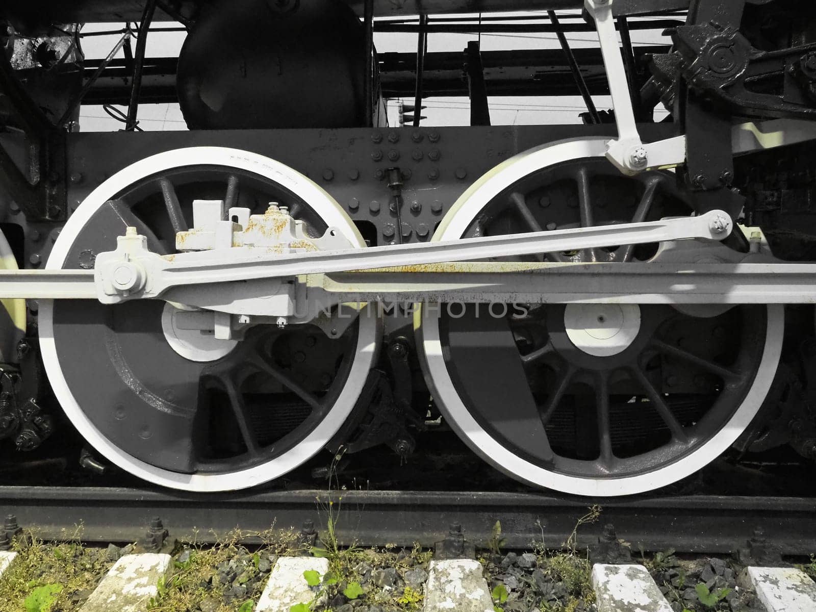 Retro train two wheels. Sleepers and rails, mechanisms, pistons and guides. Locomotive of the 19th early 20th century with a steam engine. Black and white wheels with green grass. Vintage style.