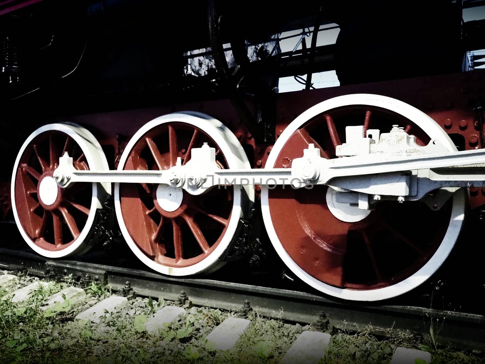 Retro vintage wheels of a locomotive or train close up. Red large heavy metal wheels with piston guiding mechanisms. Locomotive of the 19th - 20th centuries with a steam engine. Bright vivid photo.